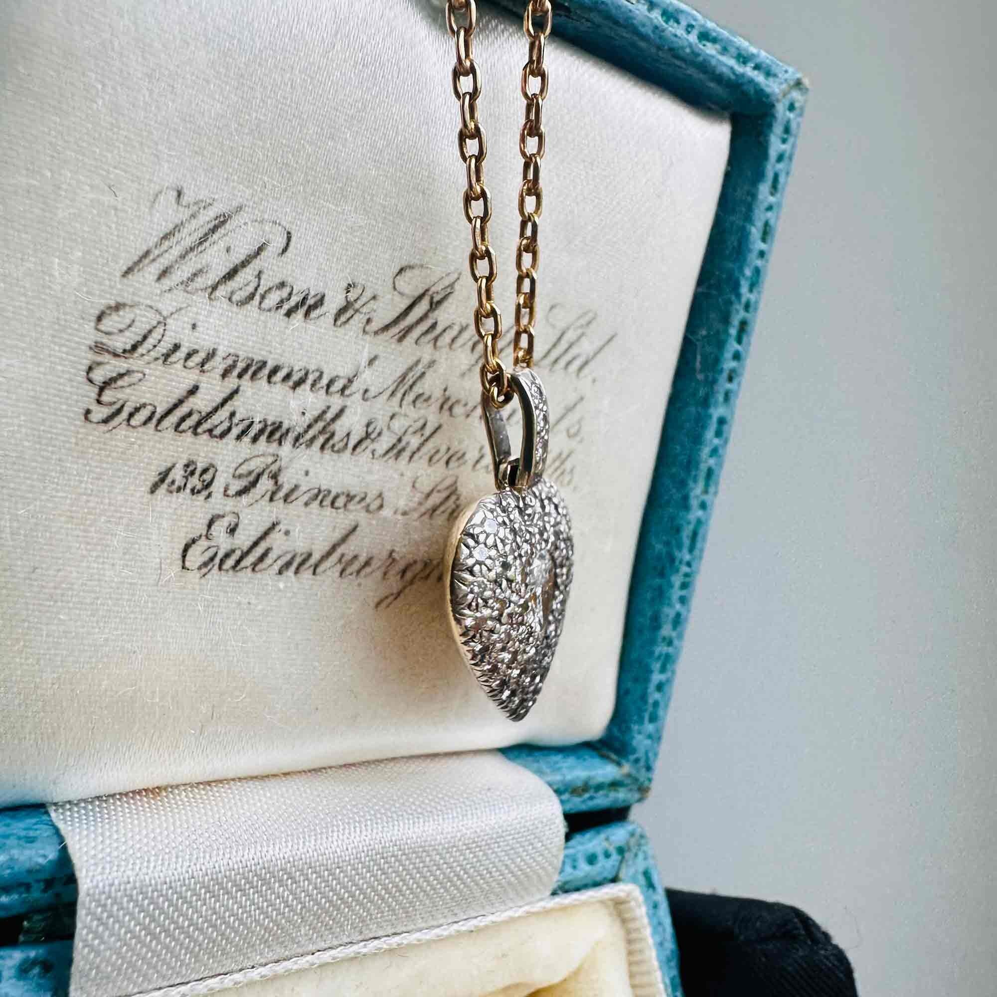 Diamond Heart Locket Pendant with Pear-Shaped Center displayed on a antique box