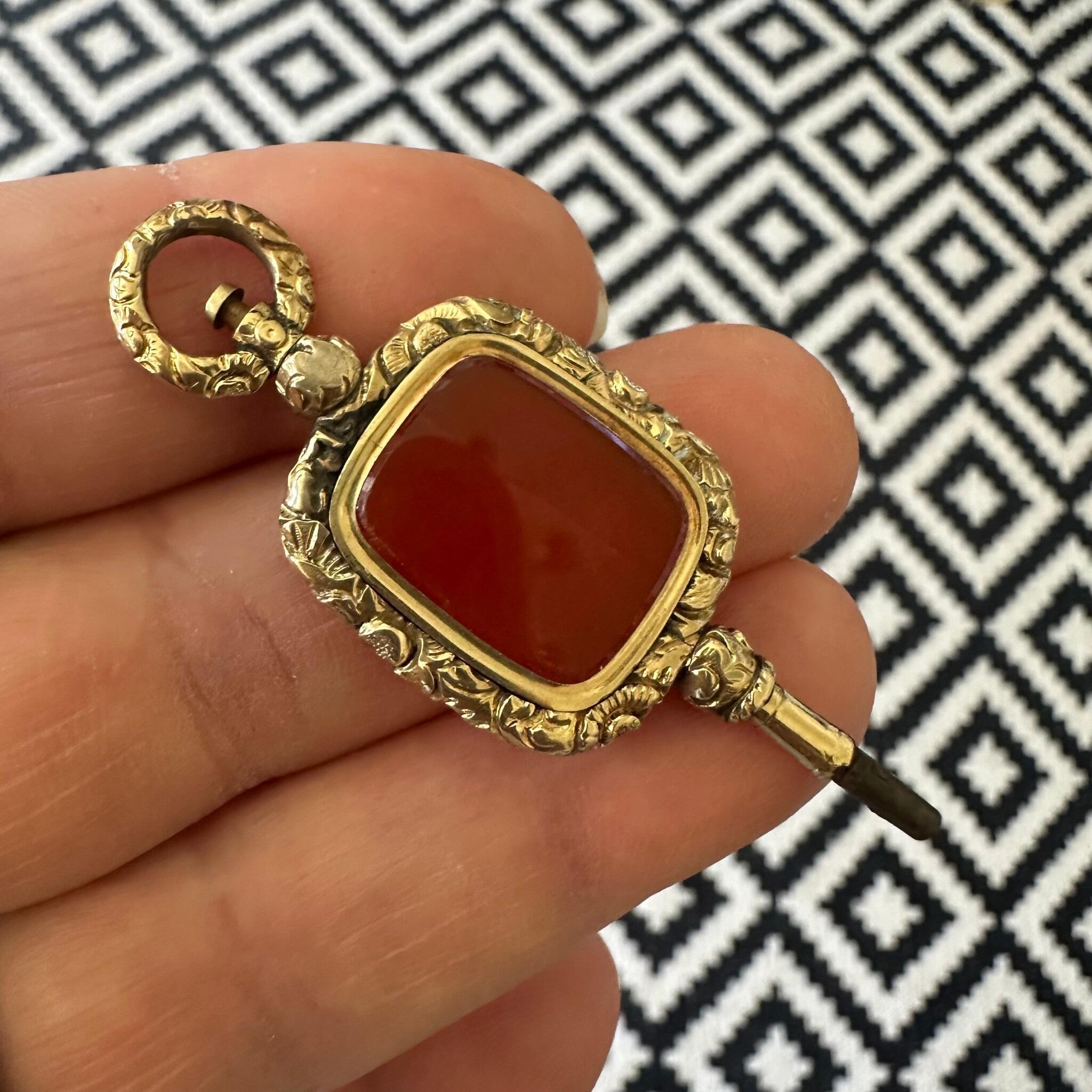 Antique Georgian Carnelian Watch Key Pendant held in hand with black and white background