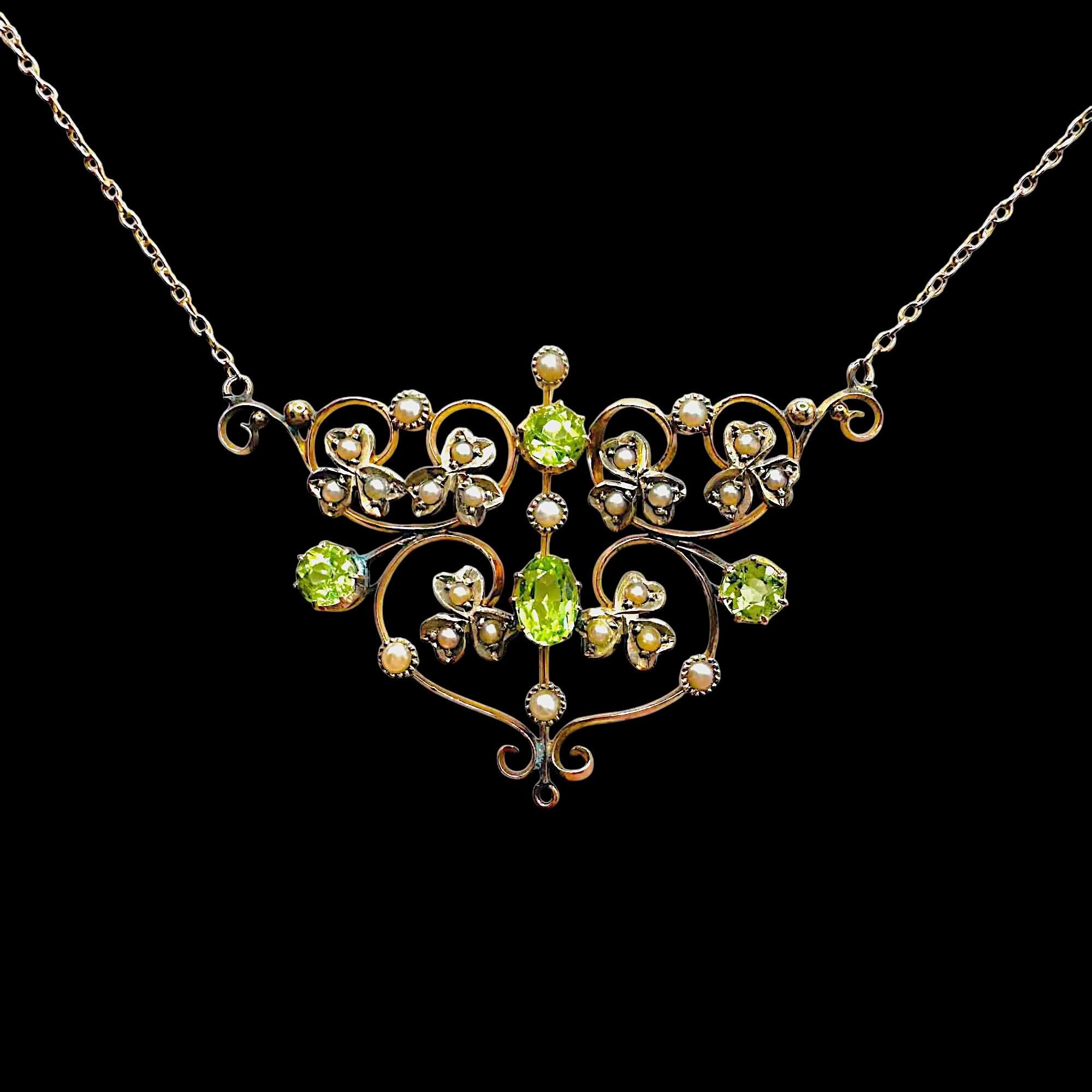 Art Nouveau 9k gold lavalier necklace with scrollwork, four peridot gemstones, and seed pearl foliate motif on black background