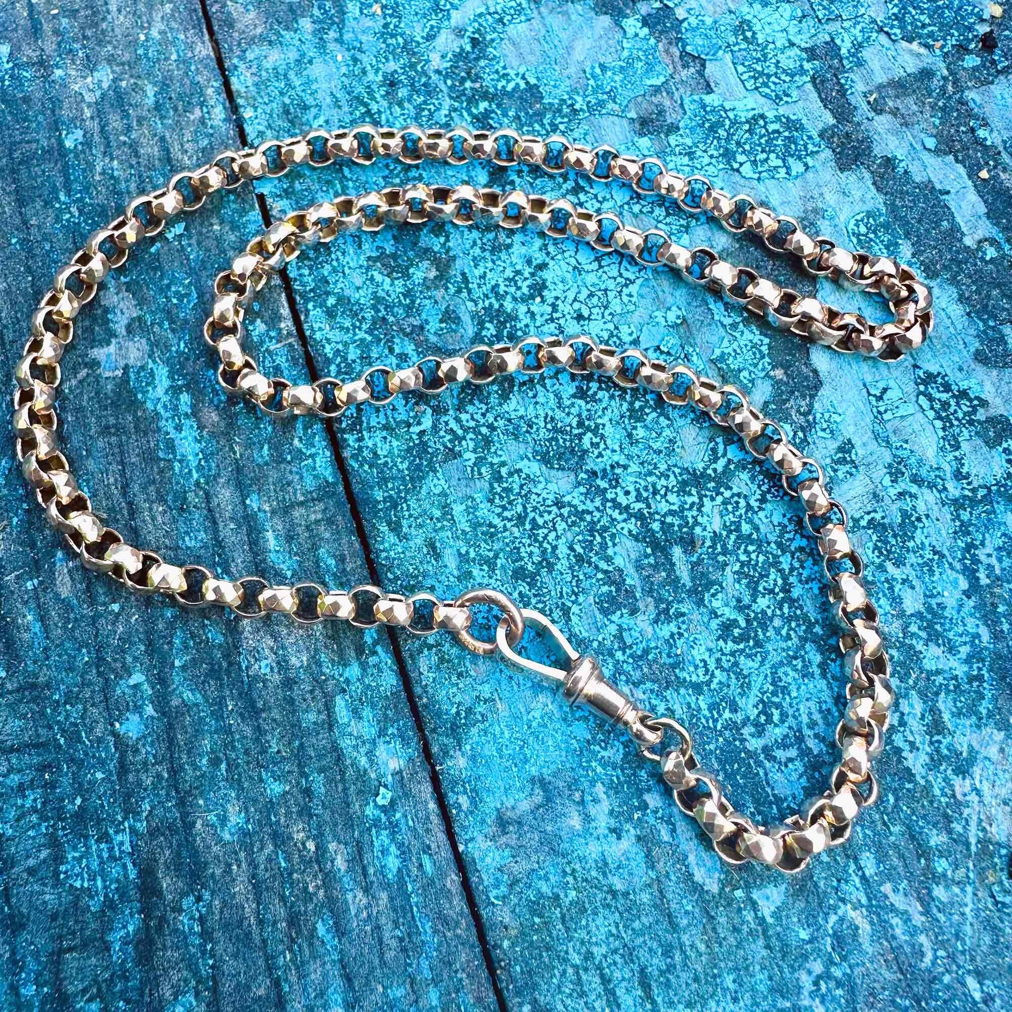 Vintage gold chain necklace with faceted belcher links, ending in an original Victorian dog clip clasp on turquoise background.