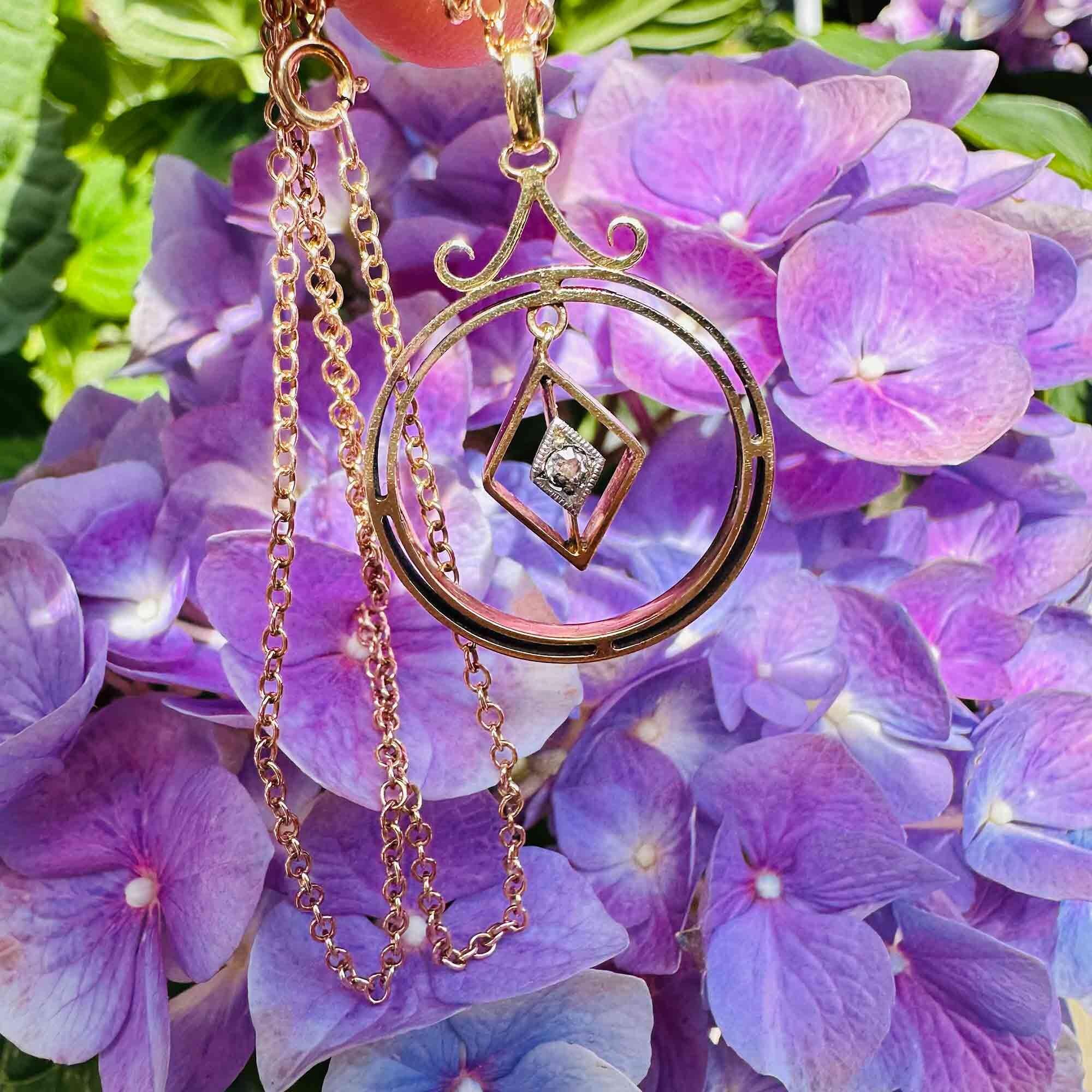 Front view of Art Deco 15k gold pendant with central diamond and geometric design, garden background.