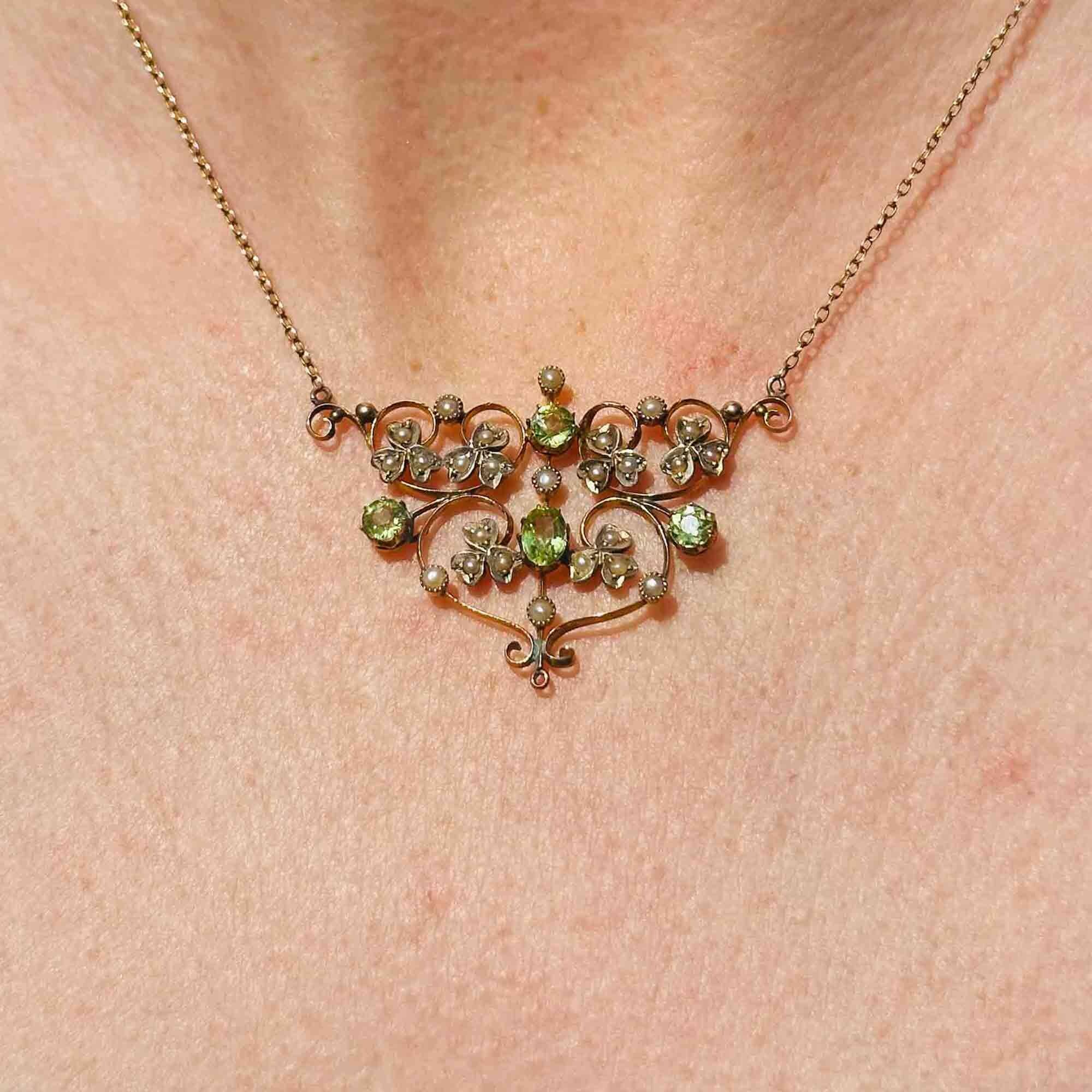 front view of Art Nouveau 9k gold lavalier necklace with scrollwork, four peridot gemstones, and seed pearl foliate motif on models neck.