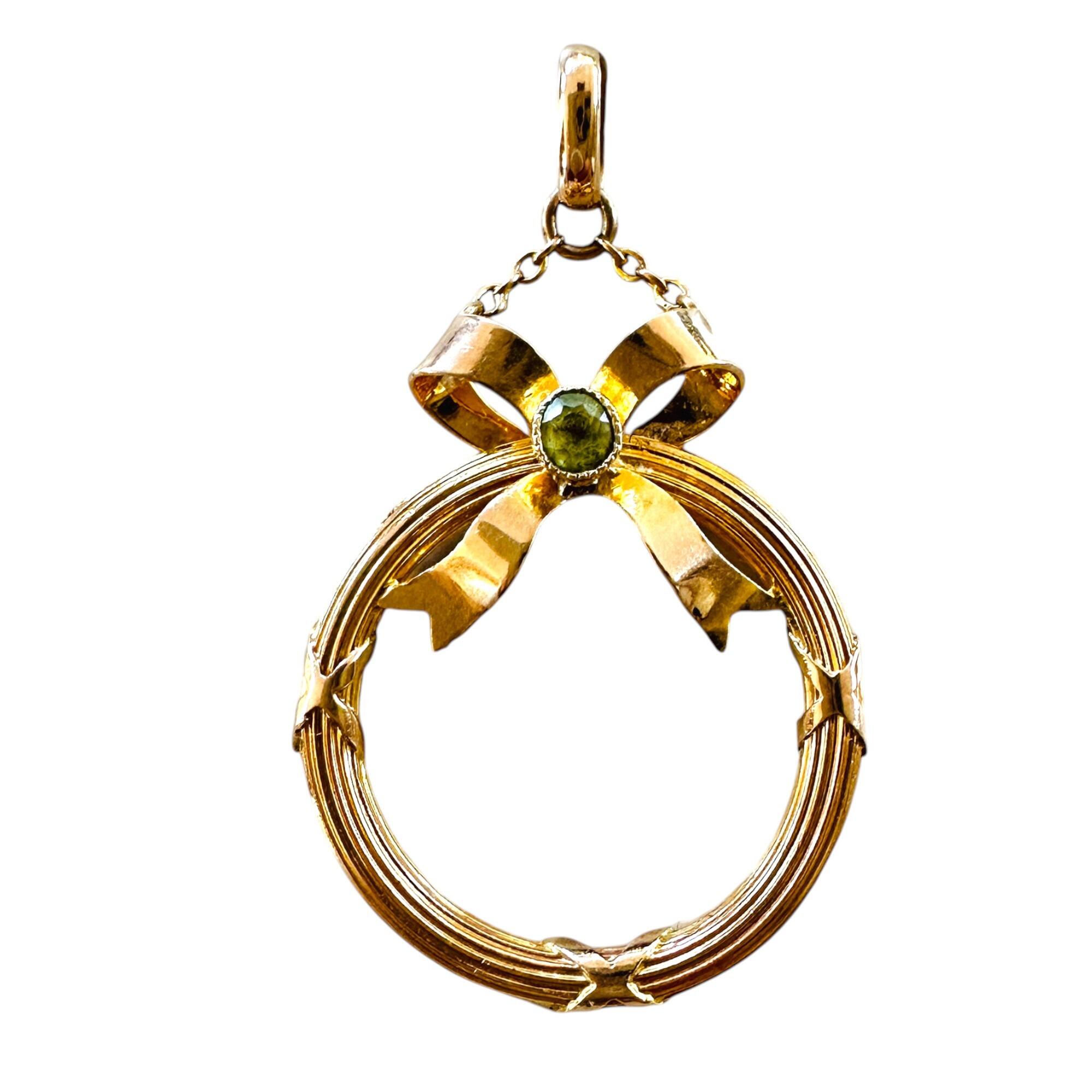 antique circular 9k gold frame pendant with peridot studded bow on white background