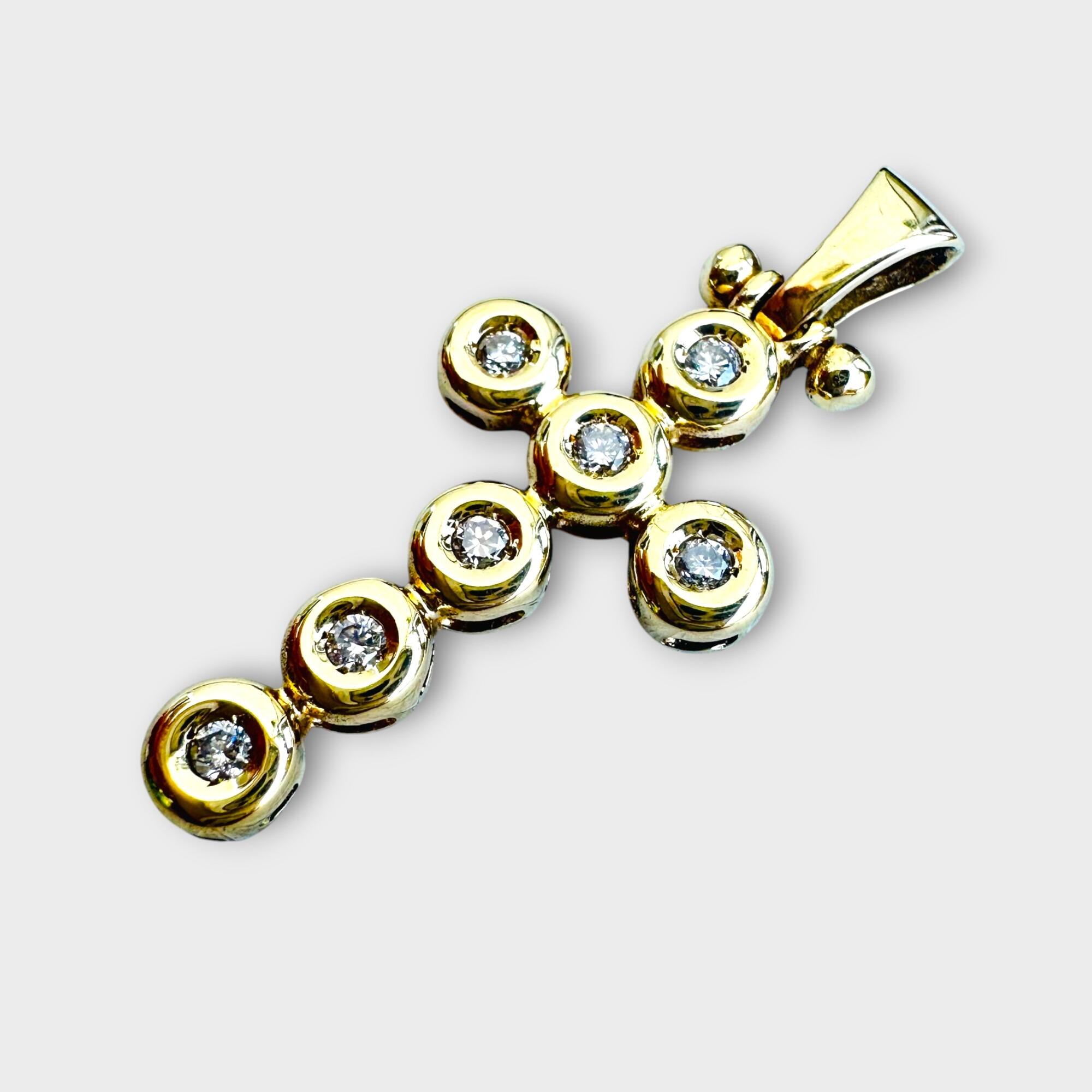 side view of 18k yellow gold and diamond cross pendant on grey background.
