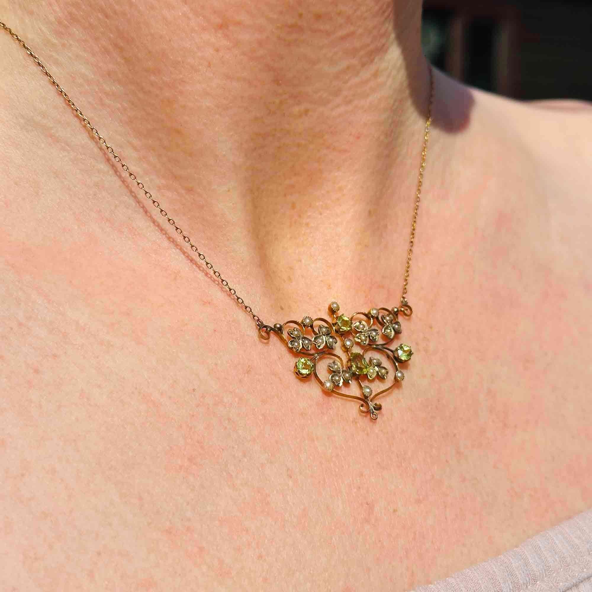 Side view of Art Nouveau 9k gold lavalier necklace with scrollwork, four peridot gemstones, and seed pearl foliate motif on models neck.