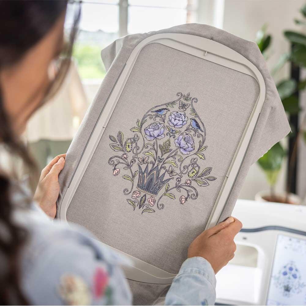 A lady hold the embroidery frame with a finished patern and the CX1e in the background