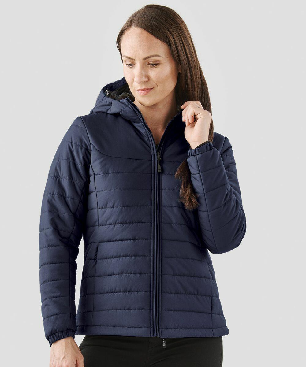 A person with long brown hair wearing a Stormtech ST213 quilted jacket is standing against a plain gray background.