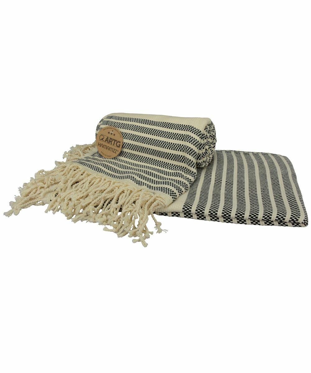 A black and white striped throw blanket with fringe detailing, partially folded, alongside a matching flat piece, featuring a brown leather label with text: AR055 by A&R Towels.
