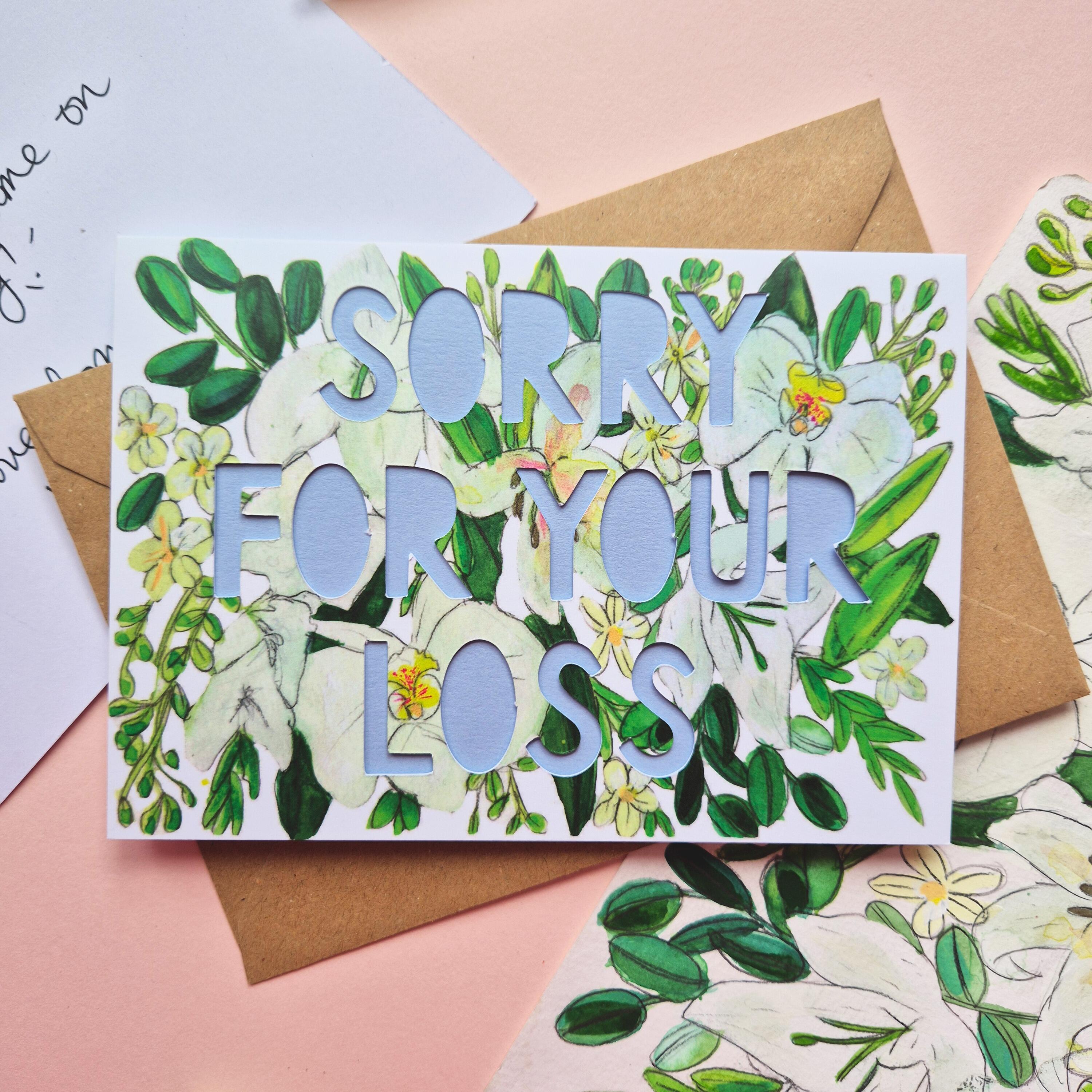 White and green floral Illustration card with die cut text that says Sorry for your loss with blue backing paper liner