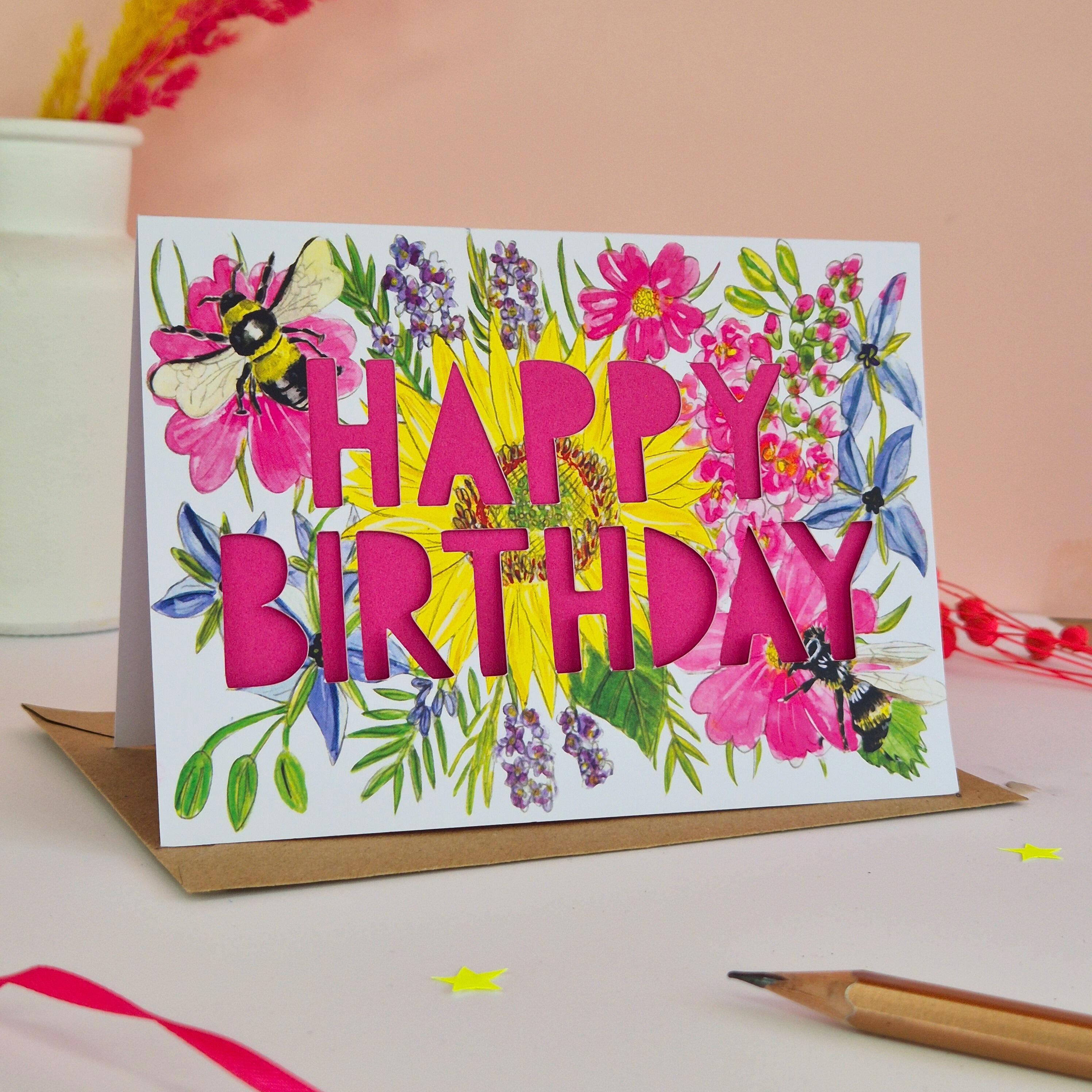 Birthday card with paper cut pink text and floral bee illustration