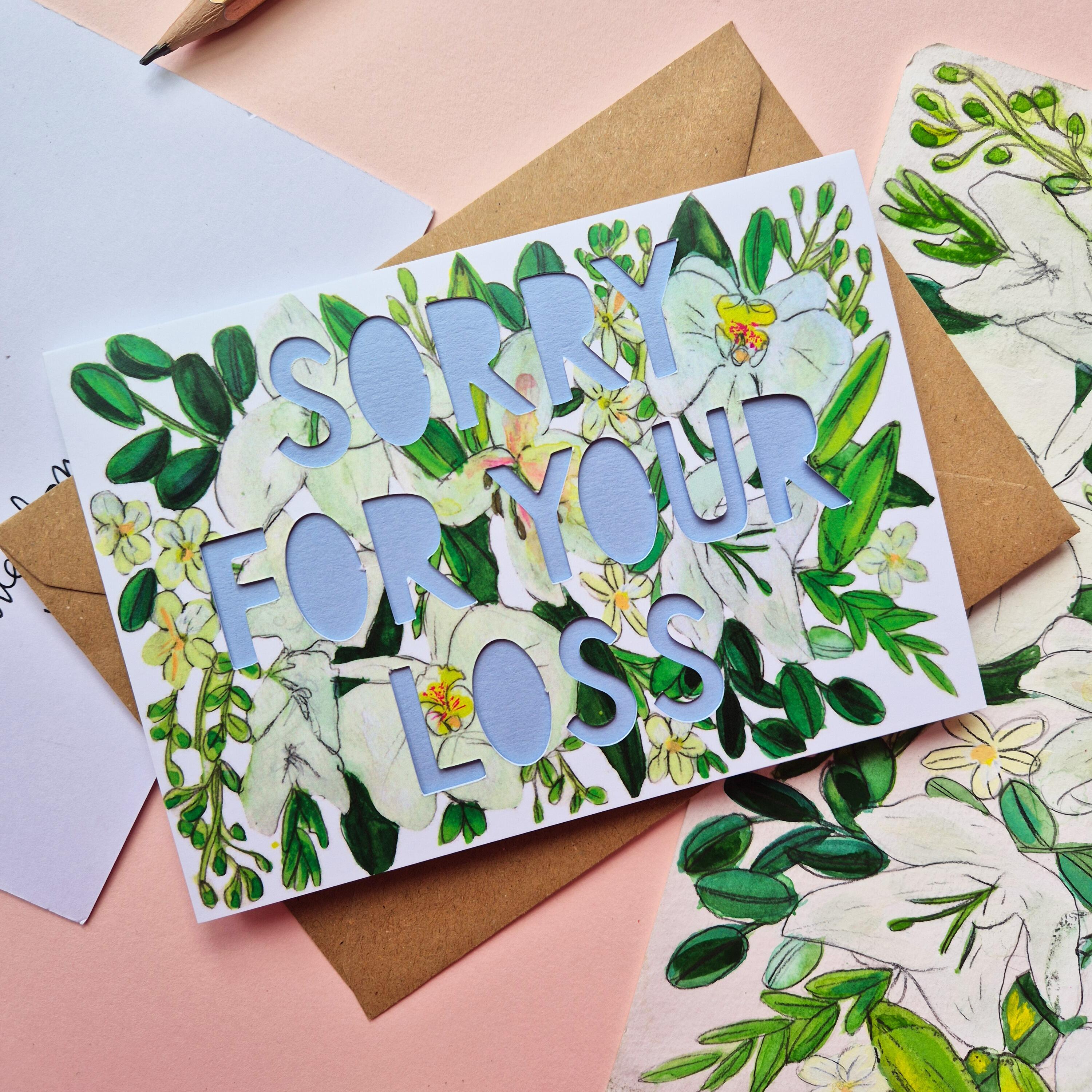 White and green floral Illustration card with die cut text that says Sorry for your loss with blue backing paper liner