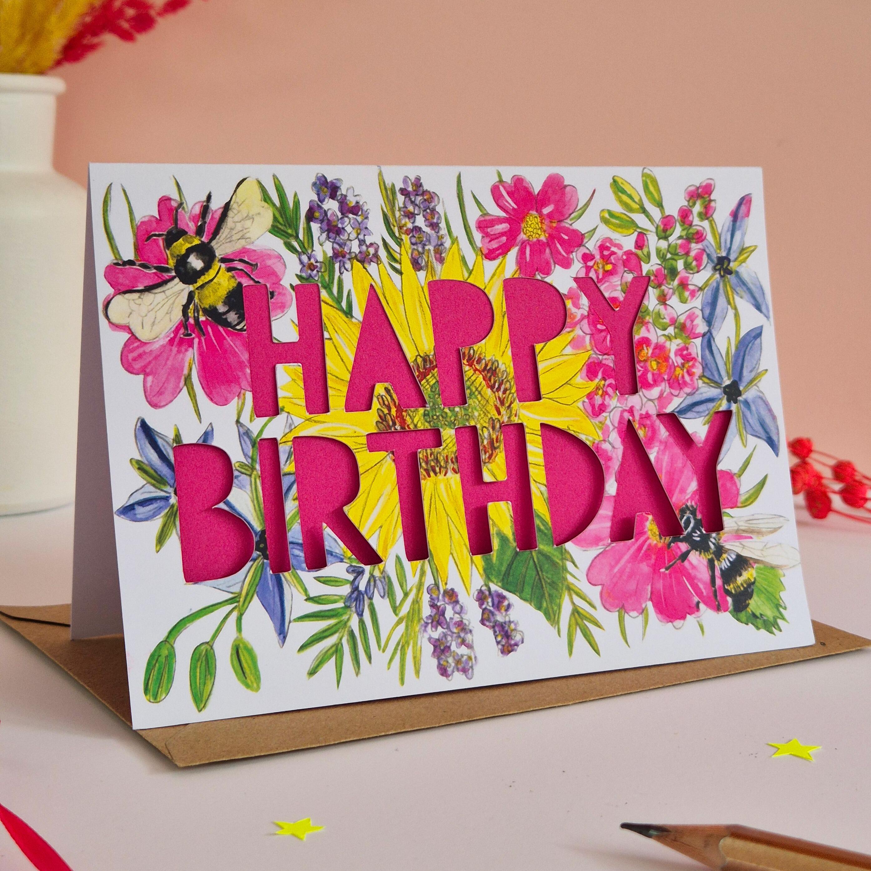Birthday card with paper cut pink text and floral bee illustration