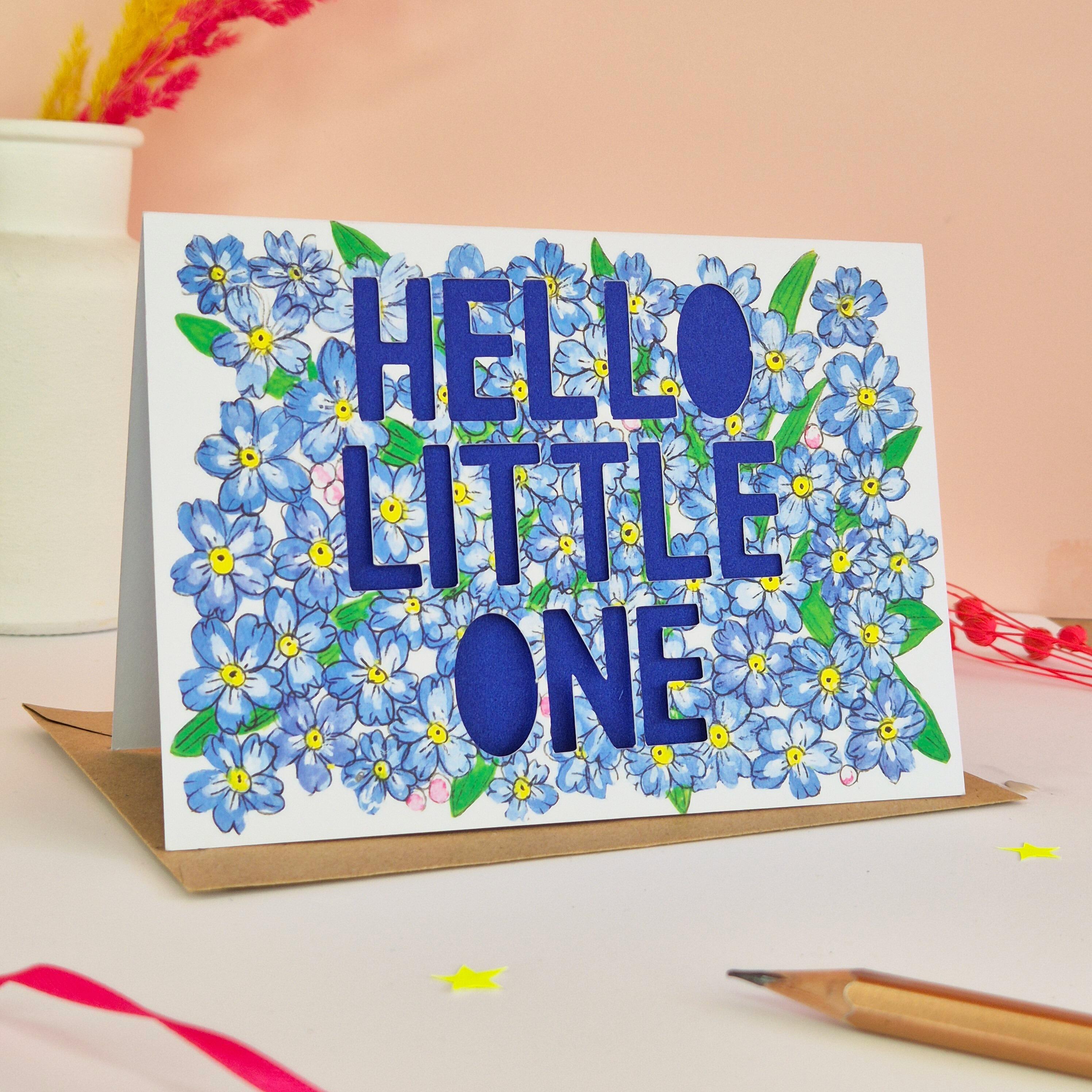 Forget-me-not floral illustration card with paper cut text that says 'Hello Little One' and bright blue backing paper