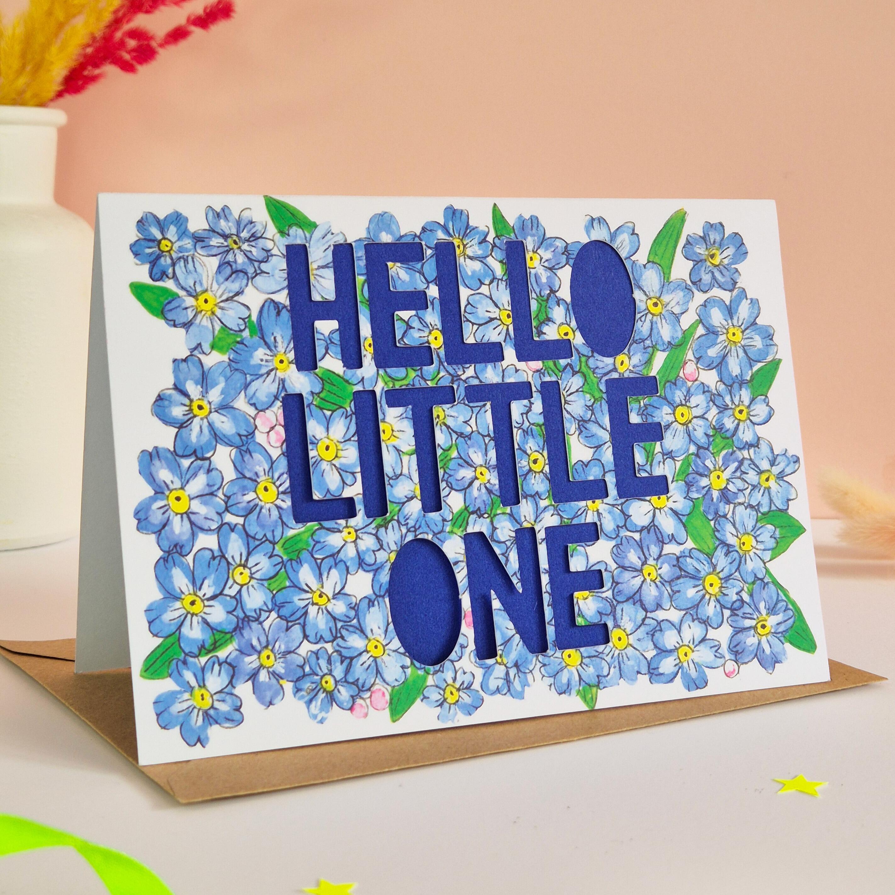 Forget-me-not floral illustration card with paper cut text that says 'Hello Little One' and bright blue backing paper