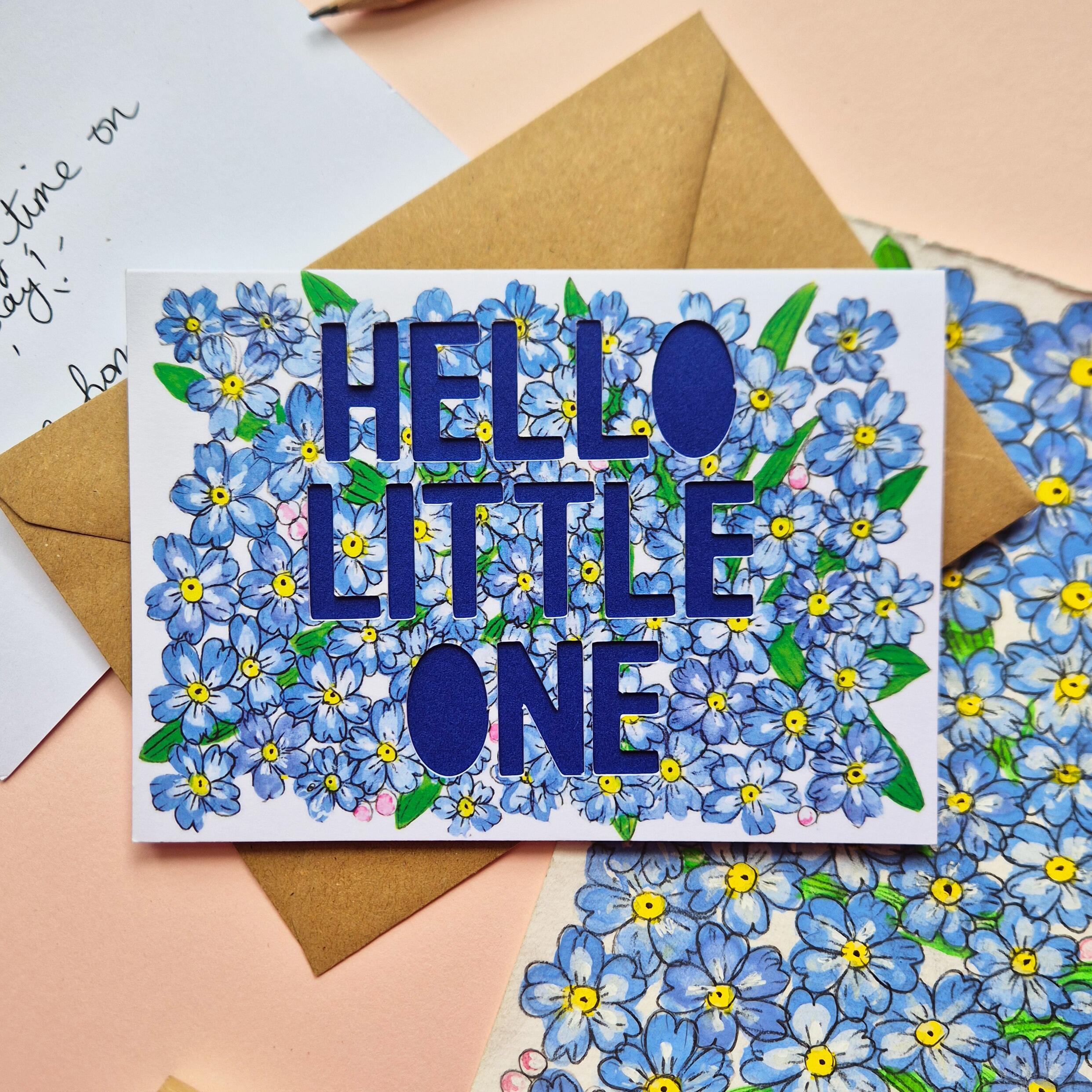Forget-me-not floral illustration card with paper cut text that says 'Hello Little One' and bright blue backing paper