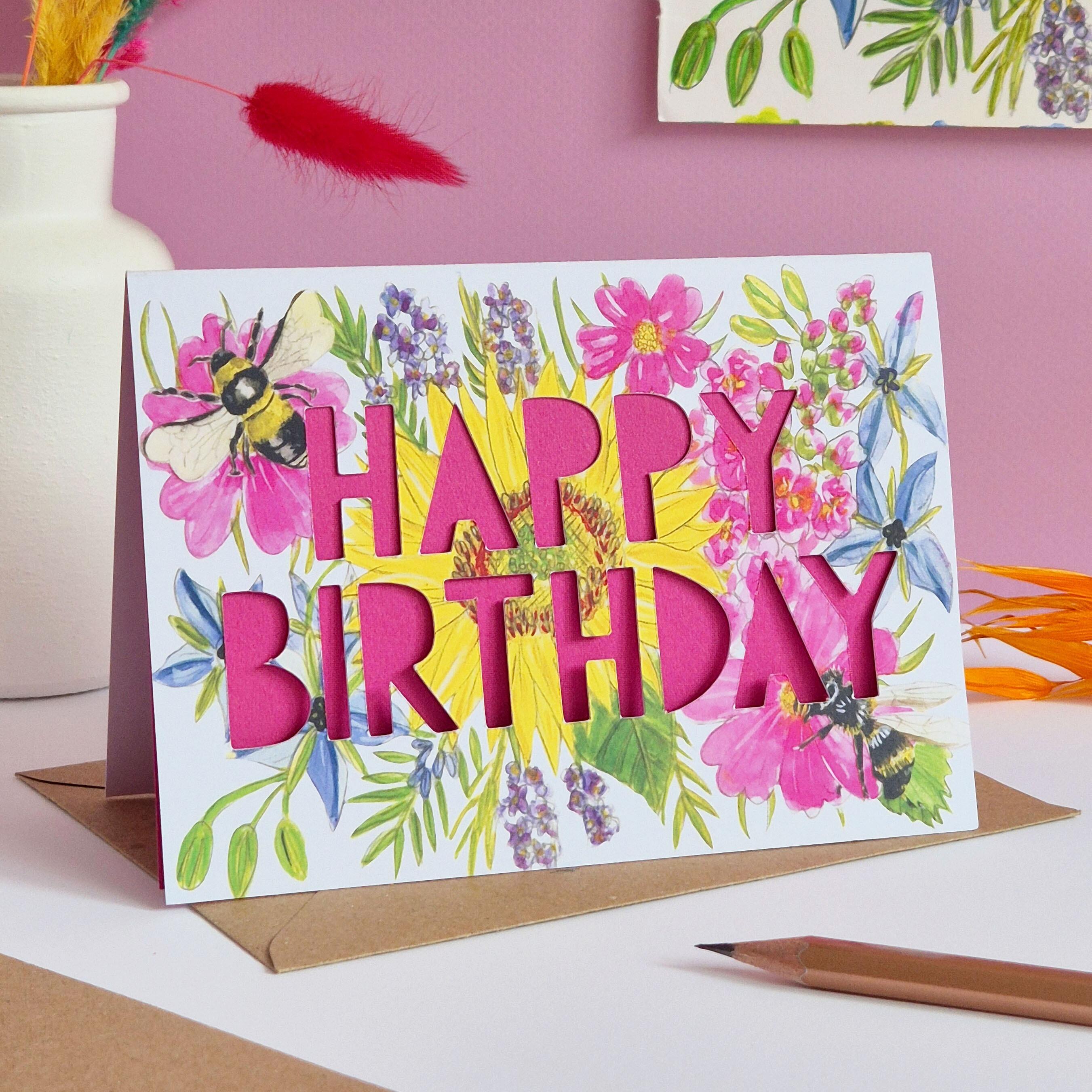 Birthday card with paper cut pink text and floral bee illustration