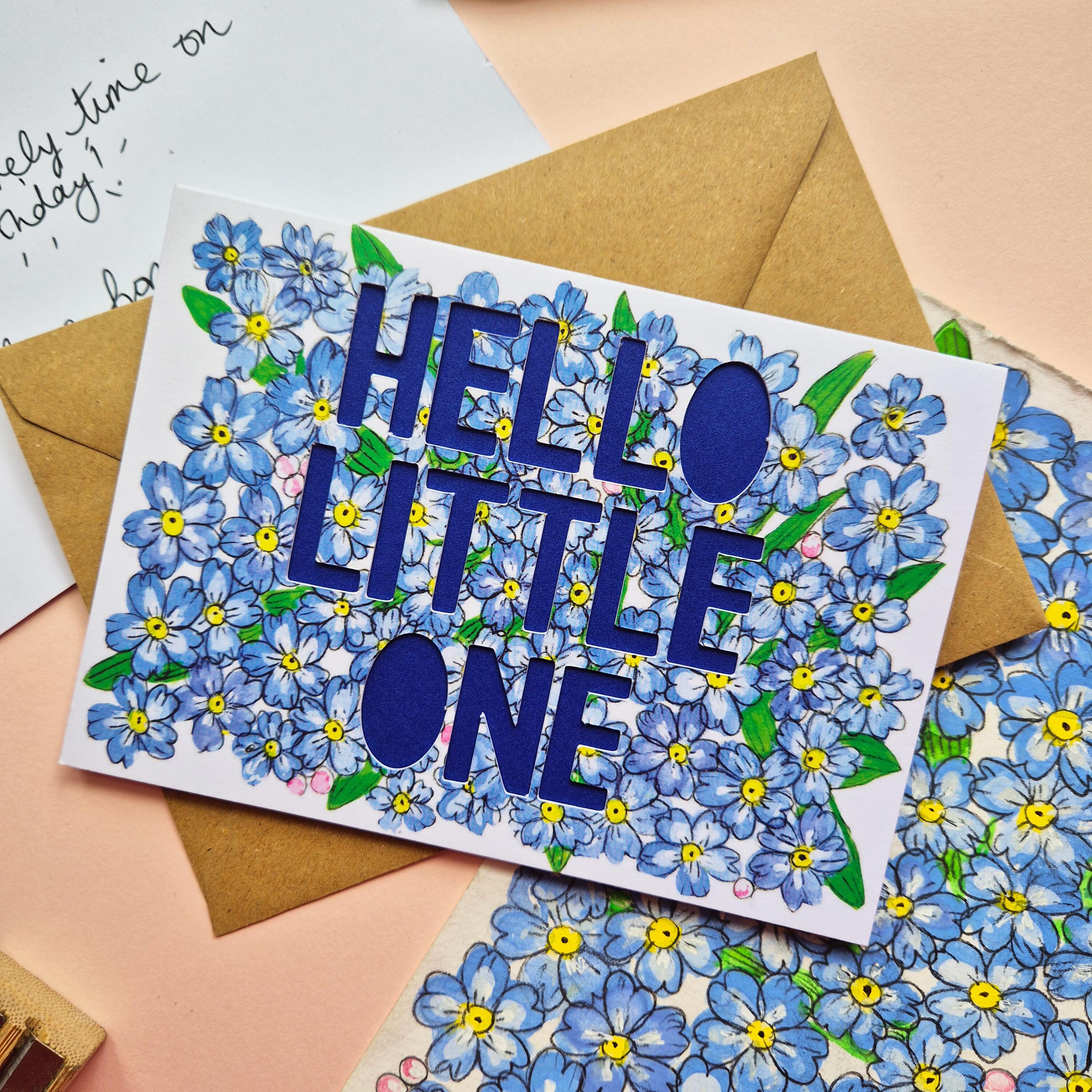 Forget-me-not floral illustration card with paper cut text that says 'Hello Little One' and bright blue backing paper