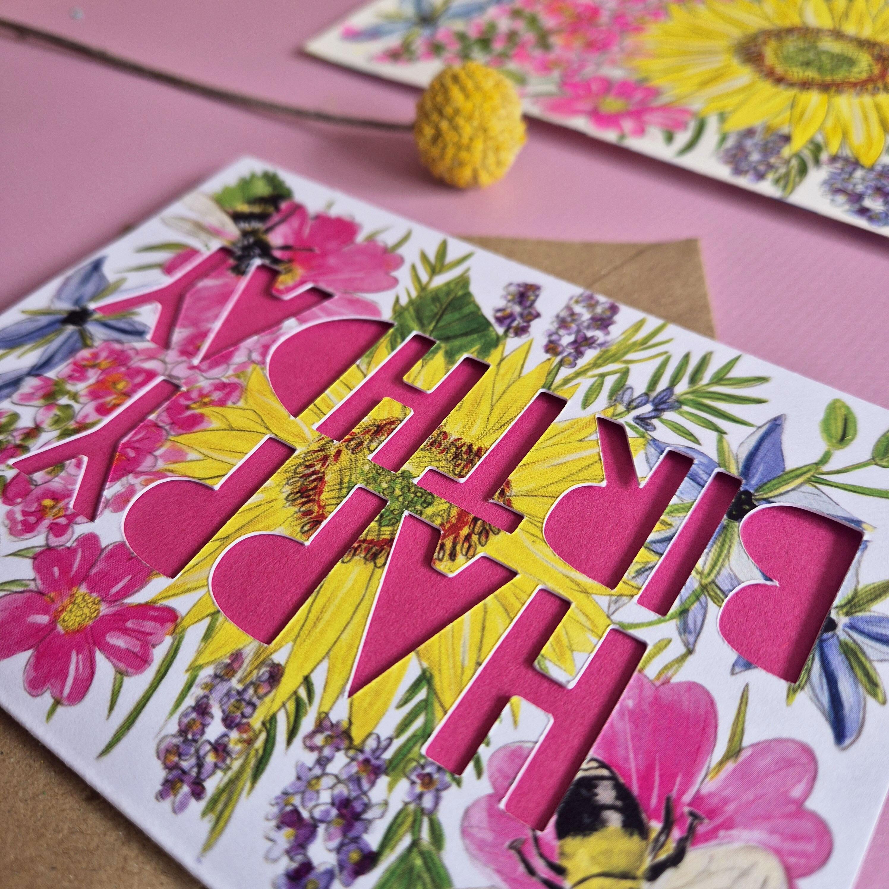 Birthday card with paper cut pink text and floral bee illustration