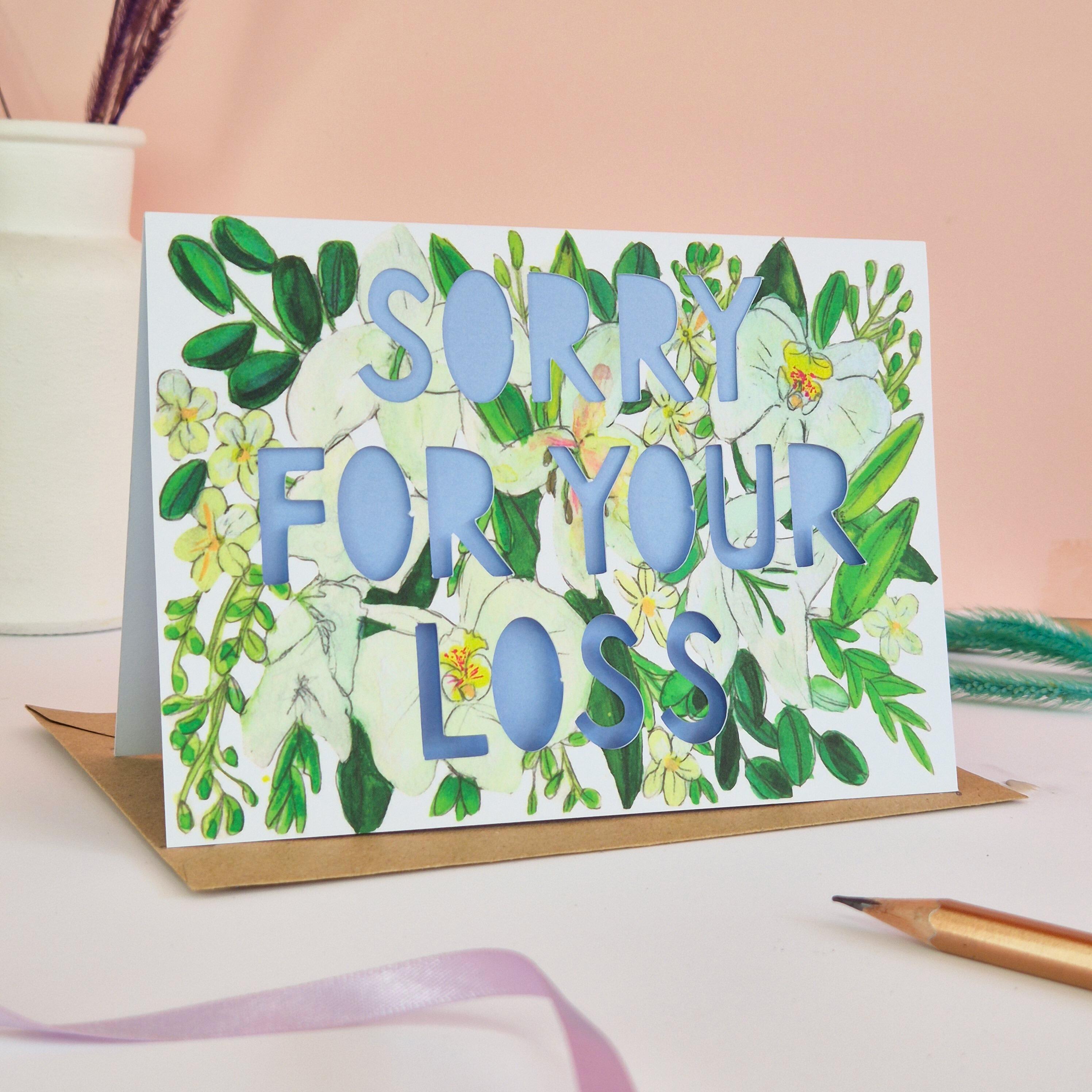 White and green floral Illustration card with die cut text that says Sorry for your loss with blue backing paper liner