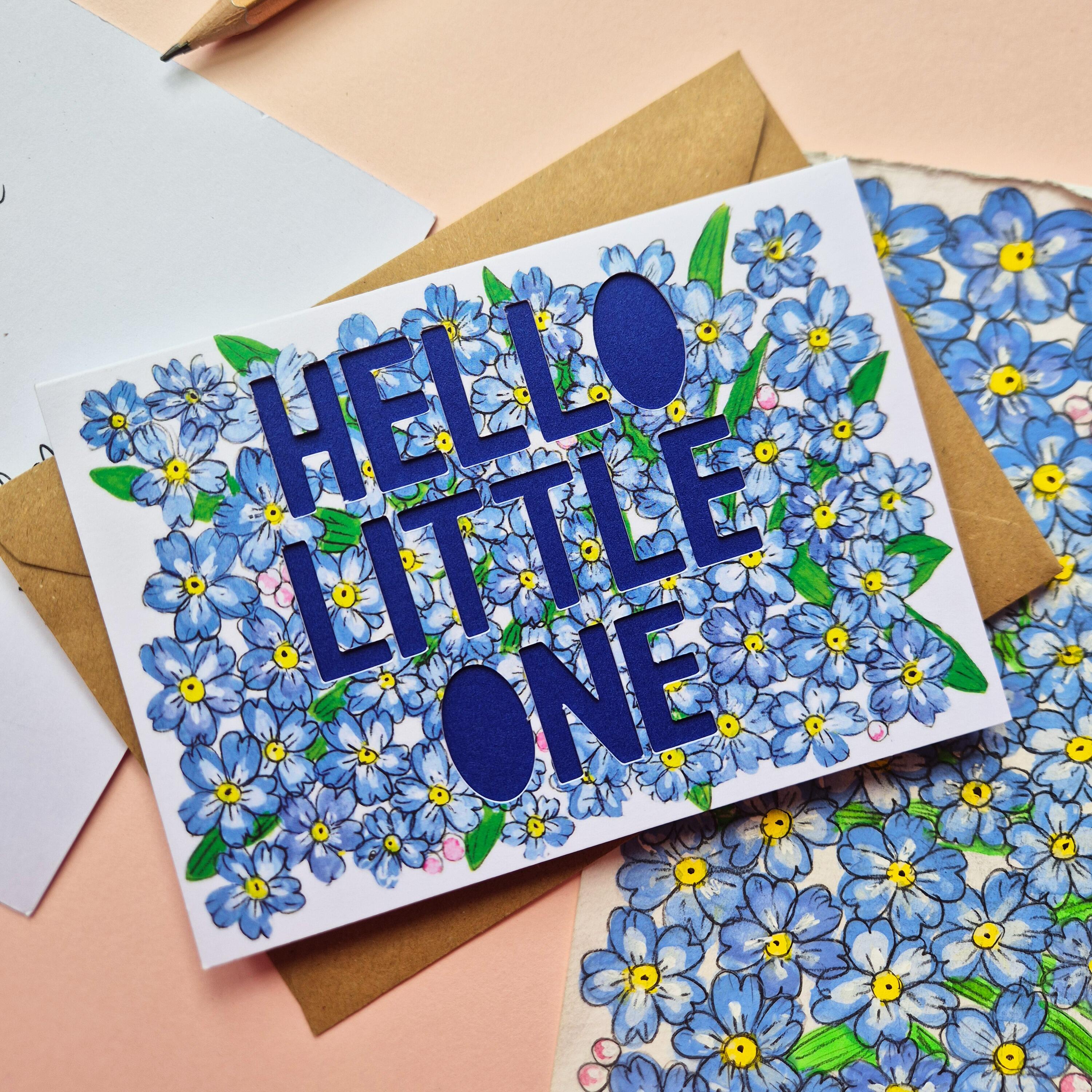Forget-me-not floral illustration card with paper cut text that says 'Hello Little One' and bright blue backing paper