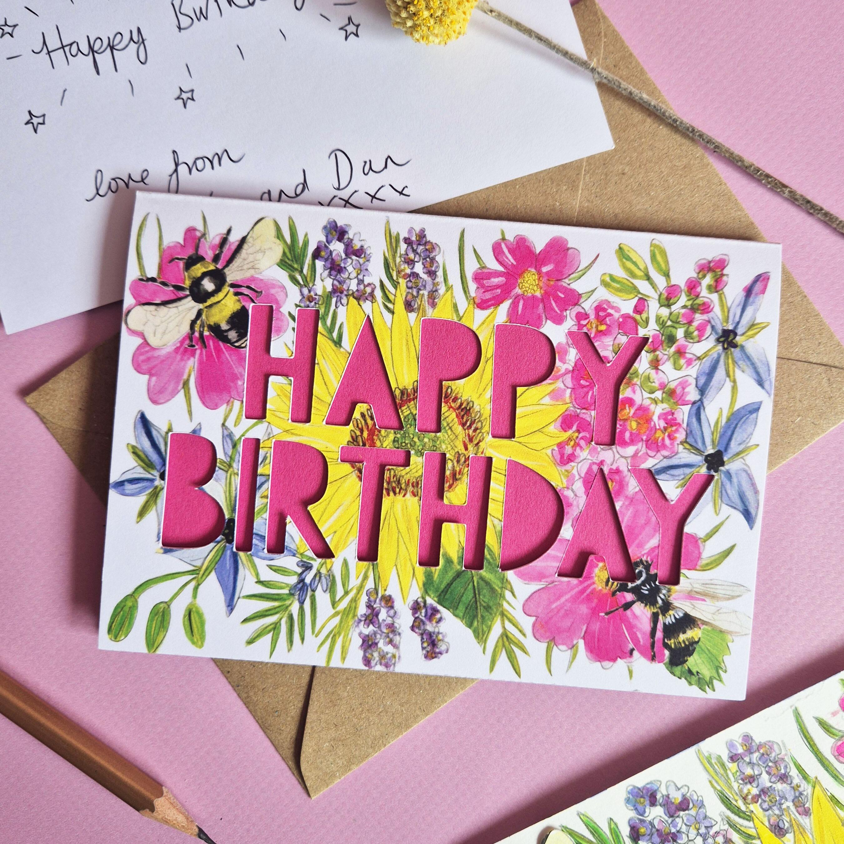 Birthday card with paper cut pink text and floral bee illustration
