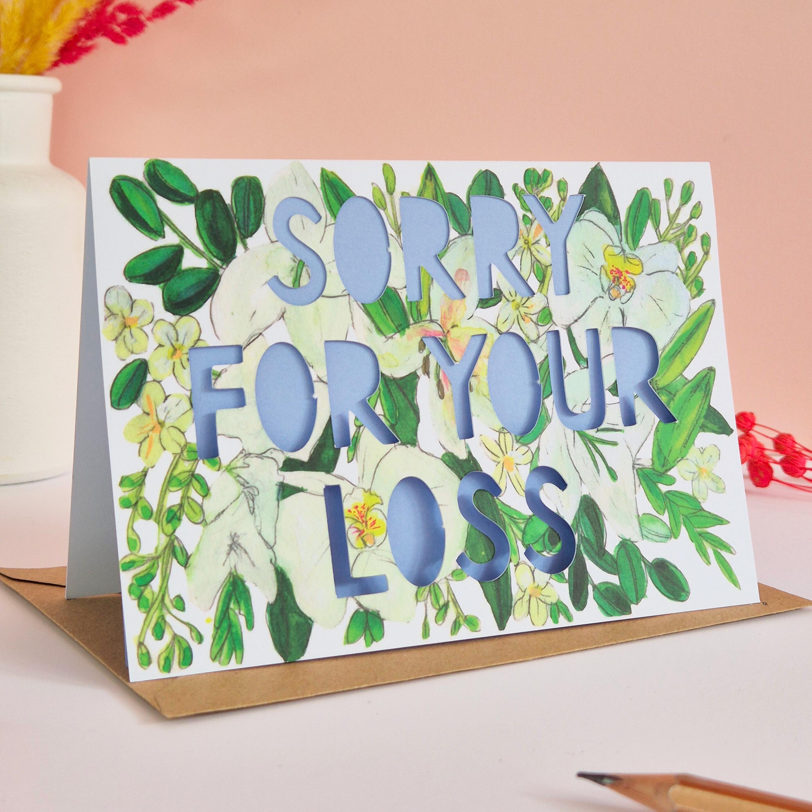 White and green floral Illustration card with die cut text that says Sorry for your loss with blue backing paper liner