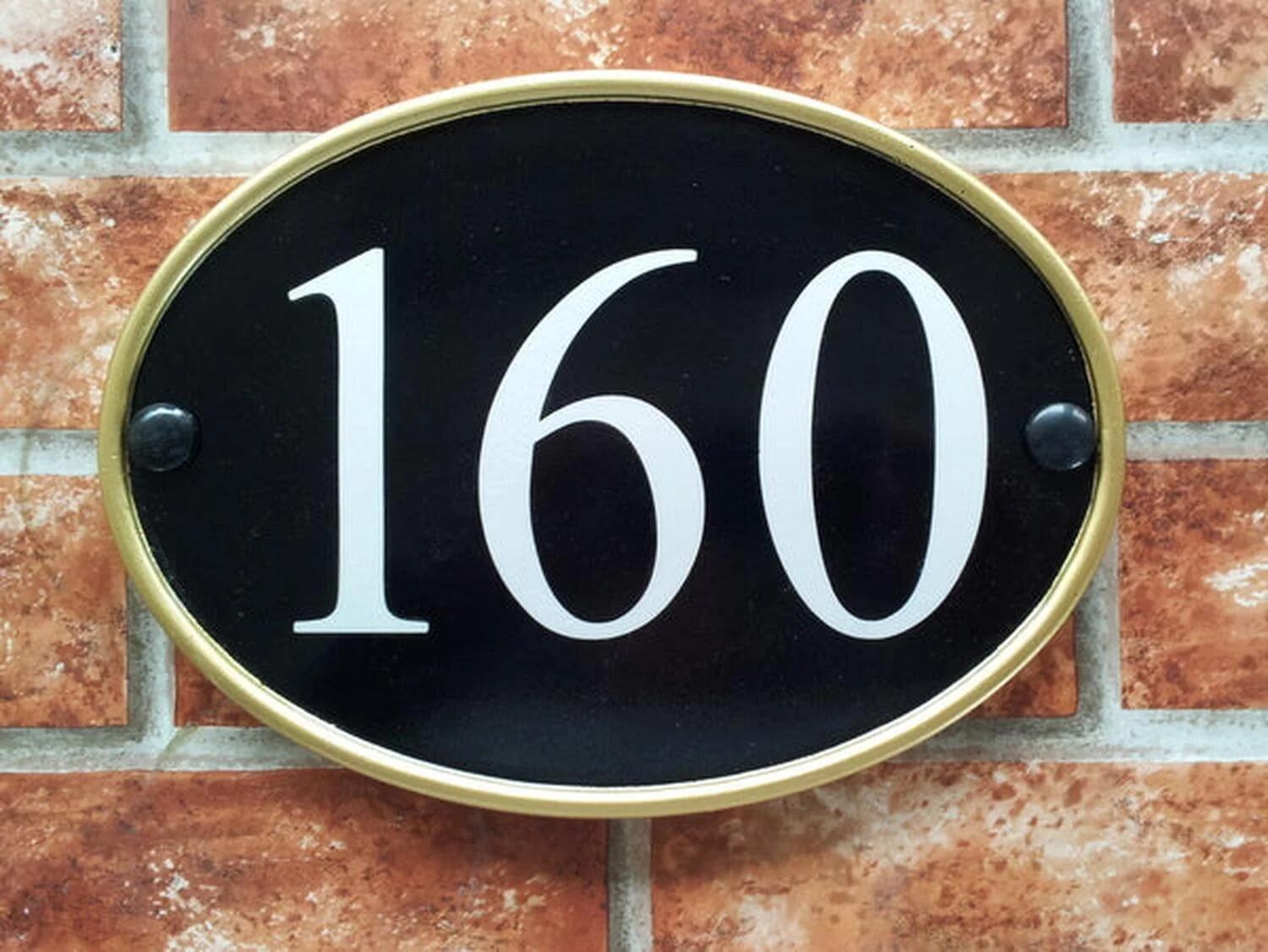 Black oval house number sign with gold rim displaying 160
