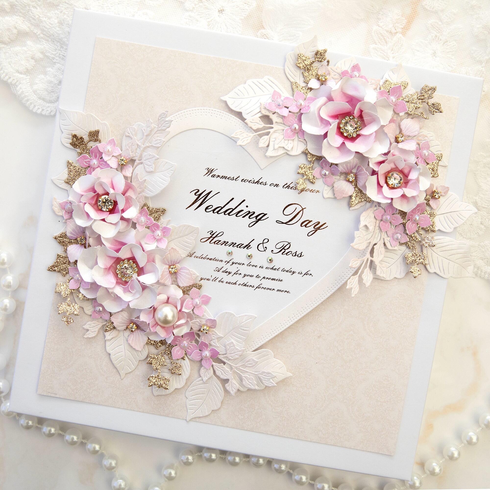 Handmade luxury personalised 8x8 wedding card with large heart topper personalised with names, surrounded by 3D blush pink paper flowers with crystal centres, white embossed leaves and gold glitter foliage, handmade in Leicestershire UK.