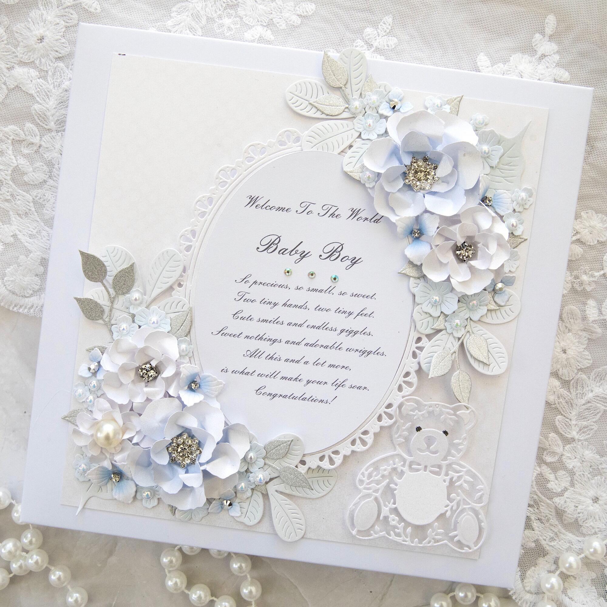 Luxury handmade personalised new baby boy card with 3D white and pale blue flowers, silver glitter leaves, crystals, pearls, lace oval frame and die-cut teddy bear, gift boxed, handmade in Leicestershire UK