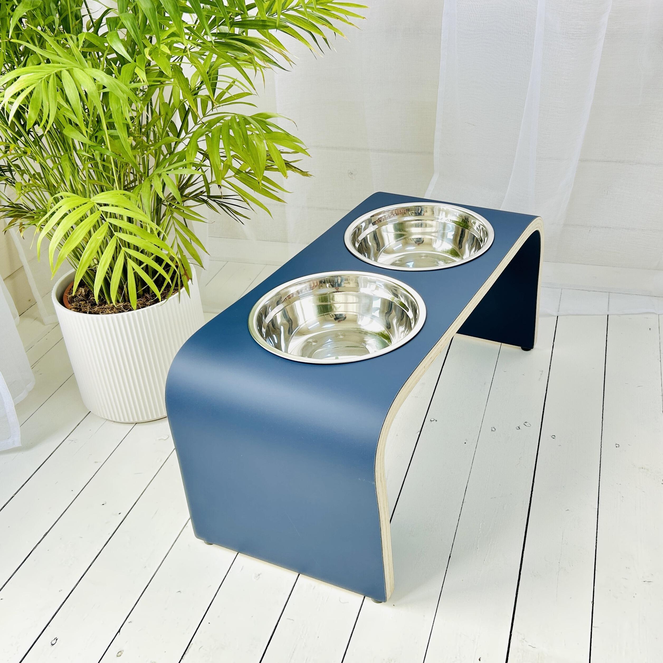 matt blue wooden dog bowl holder with two stainless steel bowls positioned on white wooden floor