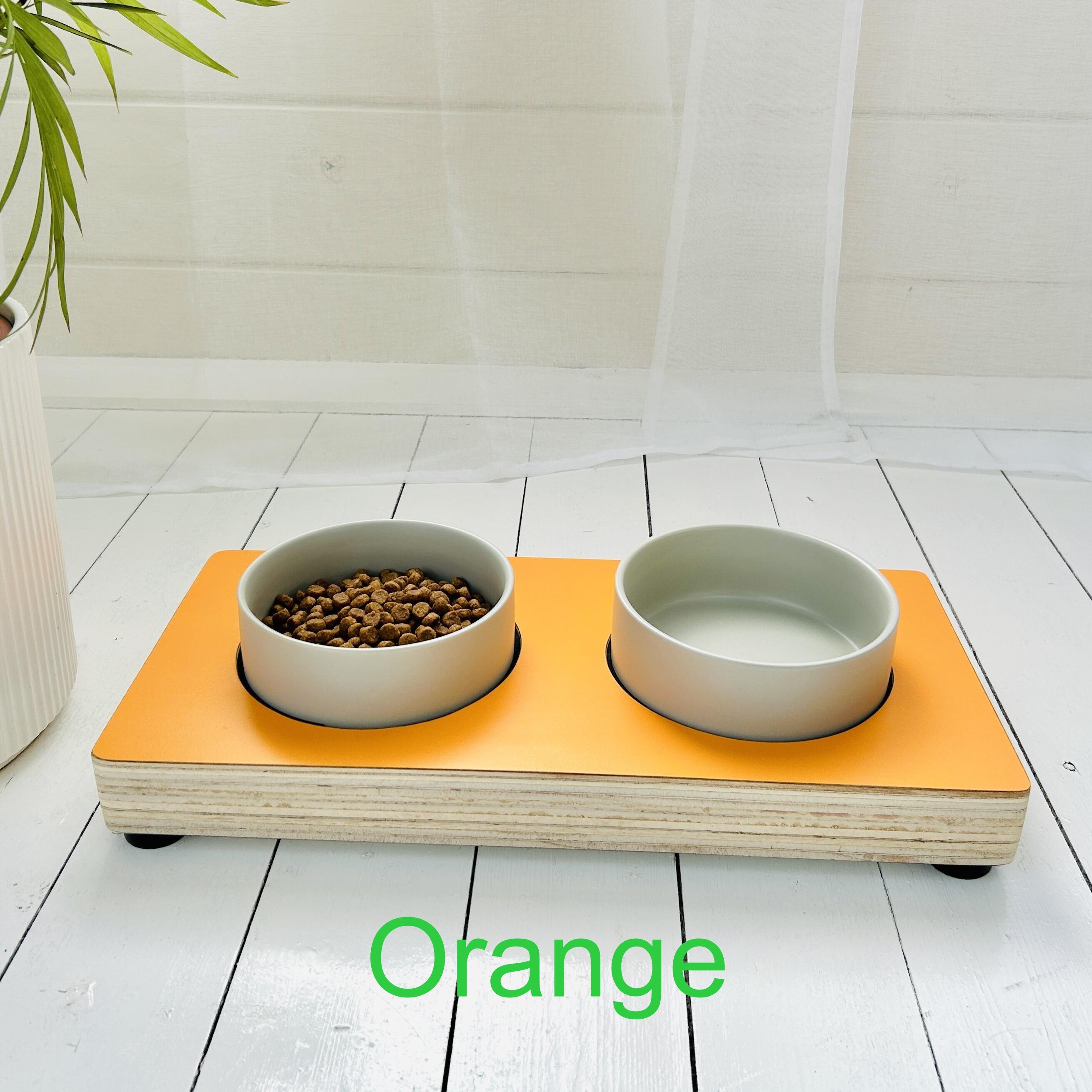 orange coloured wooden pet feeding station with grey ceramic bowls on white background