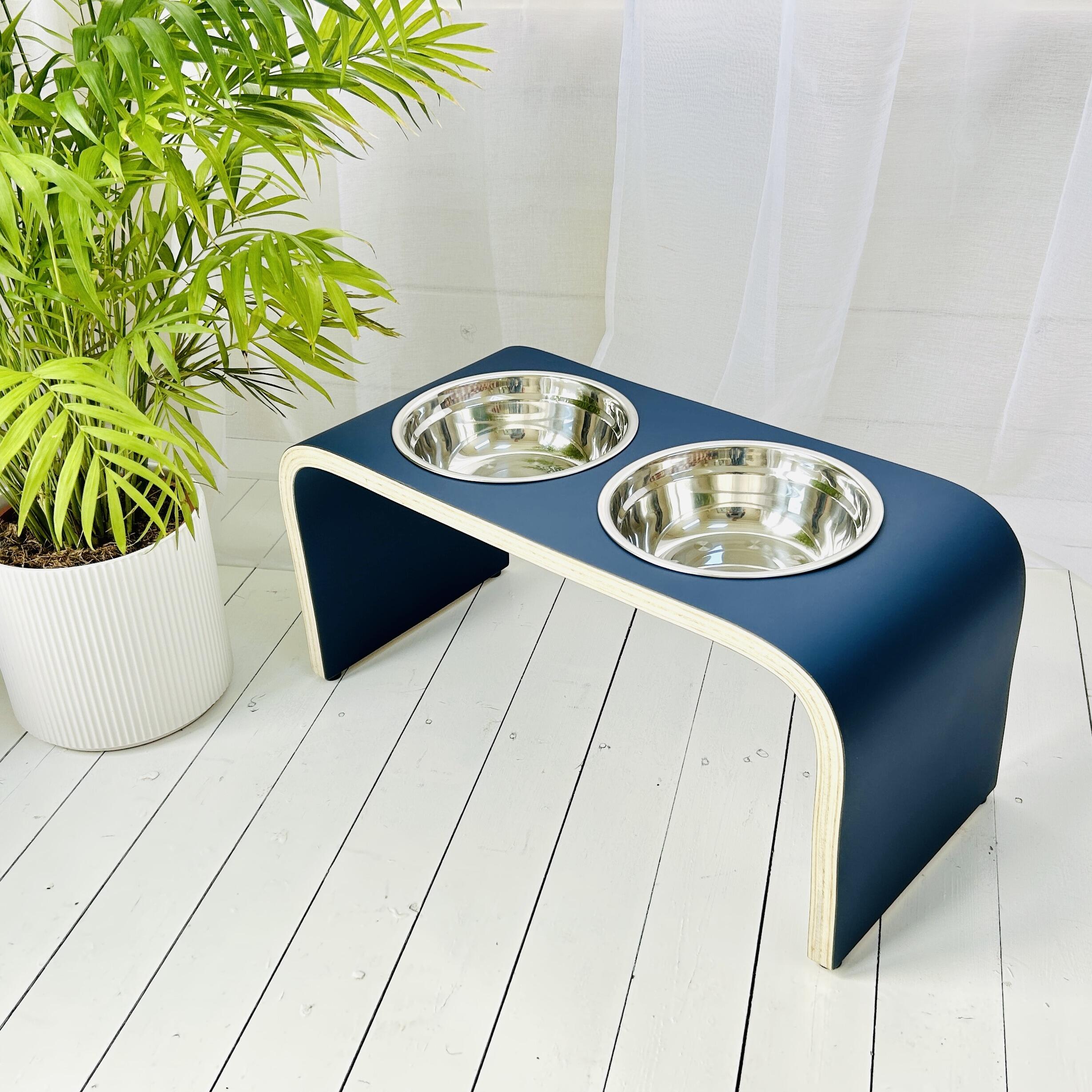 matt blue wooden dog bowl holder in white sun room with two stainless steel bowls