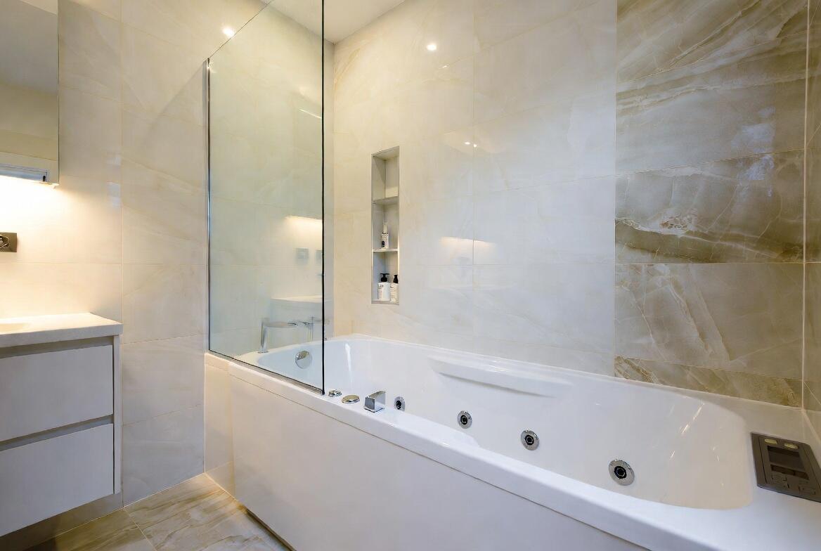 Compact modern ensuite with small whirlpool bath, clean lines, soft lighting and calm finishes