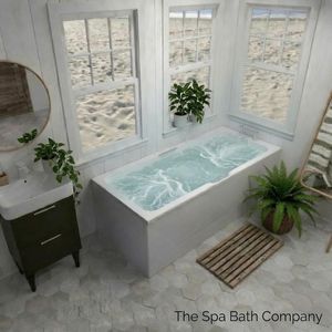 A luxury white whirpool bath surround by plants with a view of the beach through the window