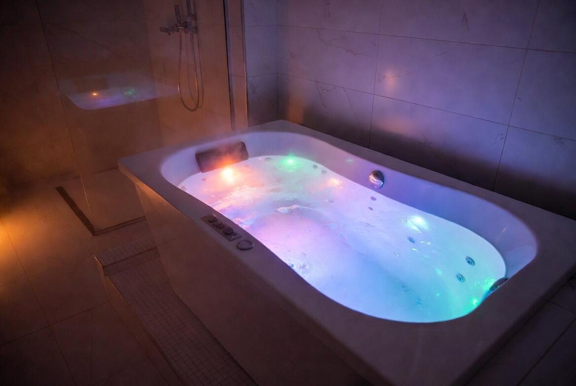Luxurious modern whirlpool bath illuminated with vibrant multi-coloured chromotherapy LED lights and steam rising, creating a premium spa atmosphere