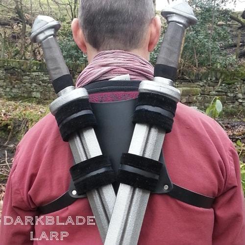 Two swords in velvet lined leather loops attached to a square piece of leather strapped to a man's back