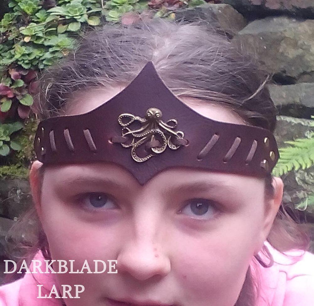 Face of a young woman wearing a brown leather headband with a brass octopus laced to it. The headband peaks to a point top and bottom on the centreline.