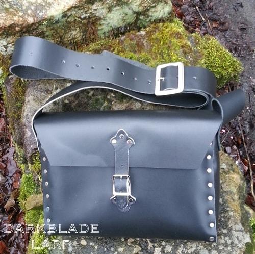 A medium sized leather satchel with a strap buckle fastening laid aginst a moss covered rock