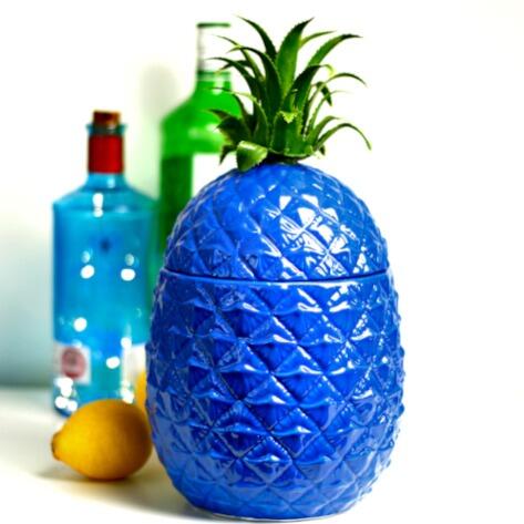 A blue pineapple ice bucket with a lemon and a home bar behind it