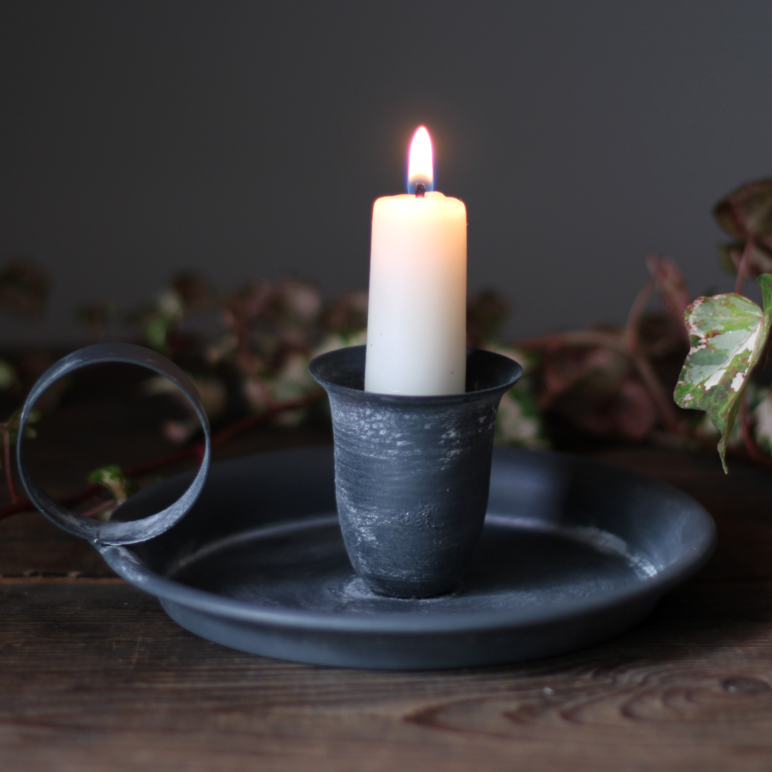 metal chamberstick holding a lit white candle in low light