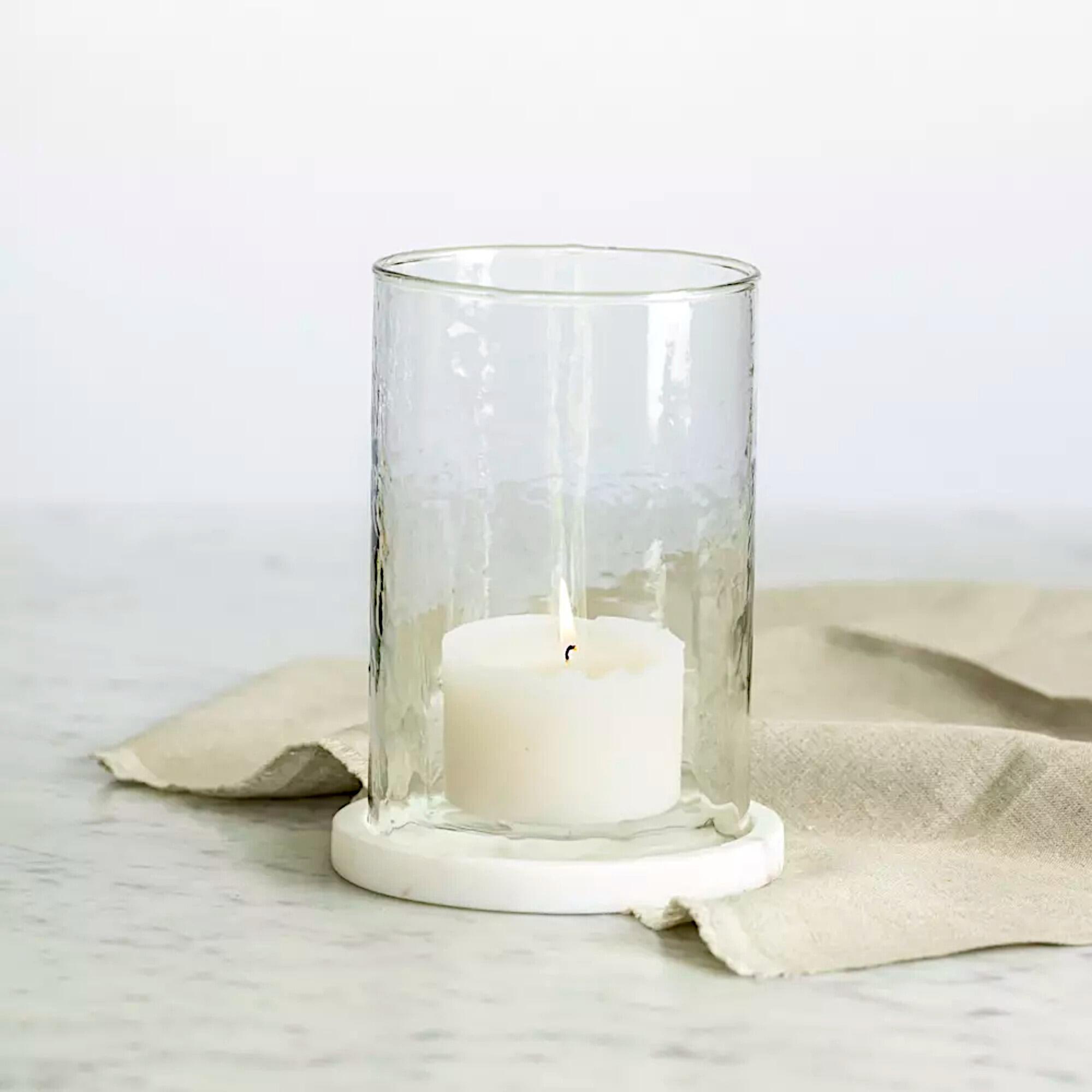 Hand-blown hammered glass hurricane lantern with a solid white marble base and a white pillar candle lit inside.