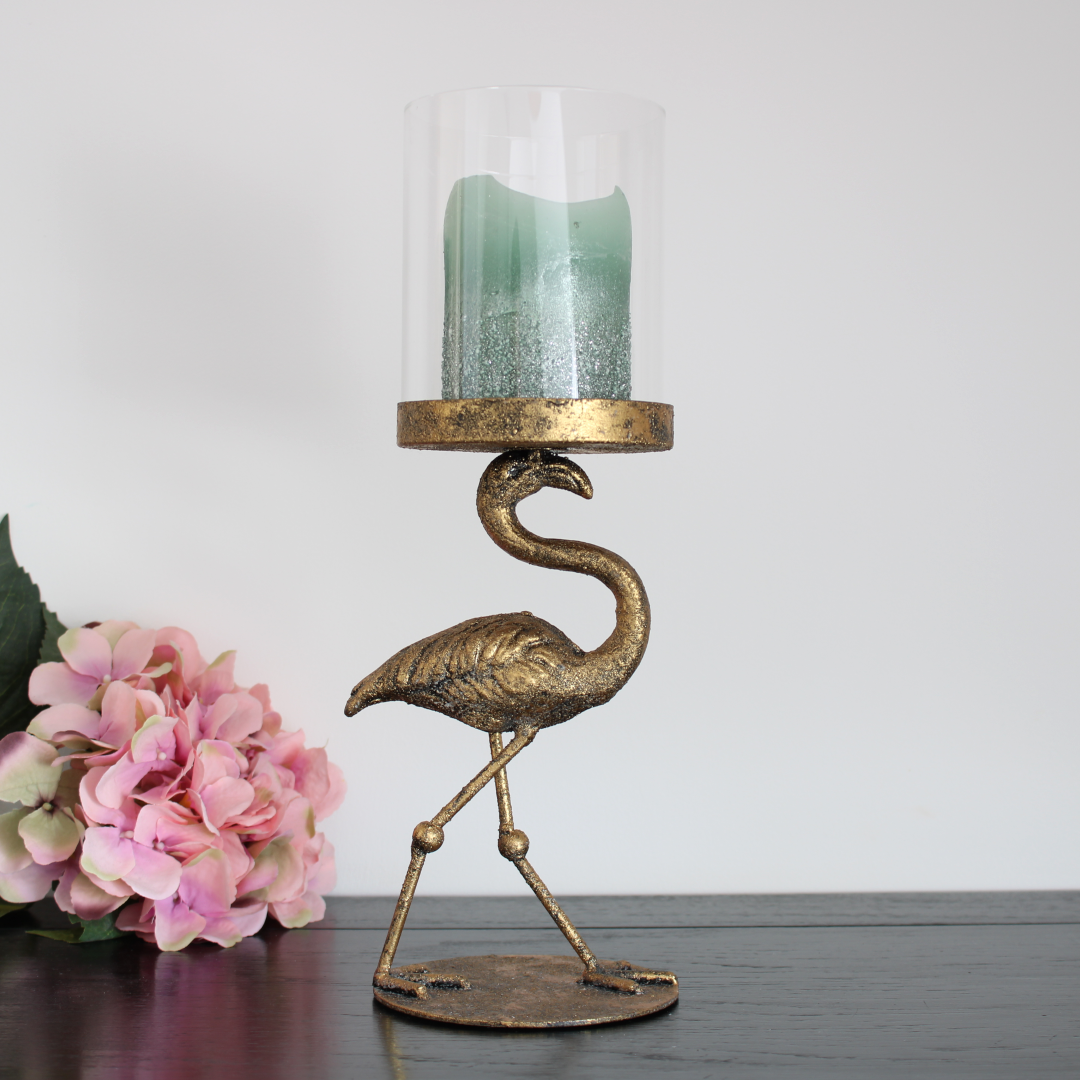 metal vintage gold pillar candle holder with glass hurricane in the shape of a flamingo with a rustic green pillar candle focusing on the right hand side.