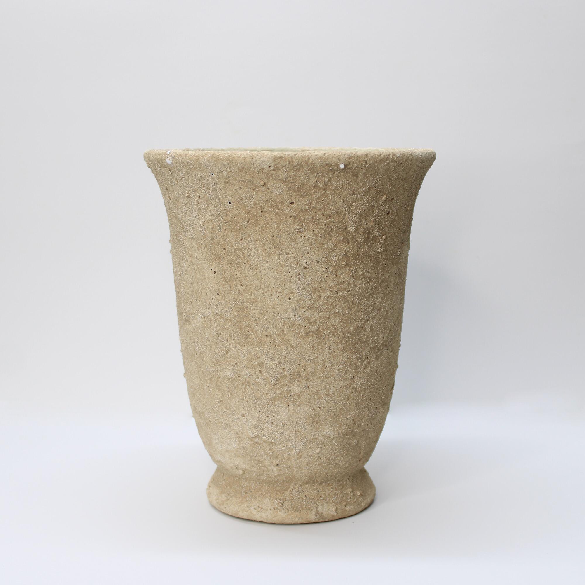Close-up of a tapered light brown cement planter with a heavily distressed sandstone texture on a white background.