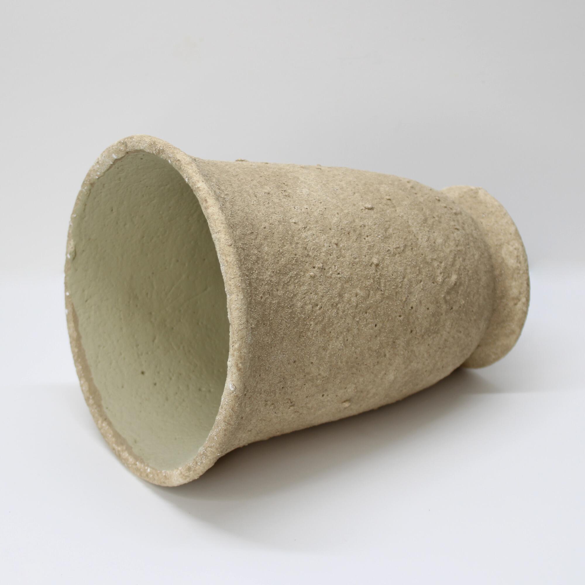 A textured cement pot with a pedestal base on its side, focusing the inside.