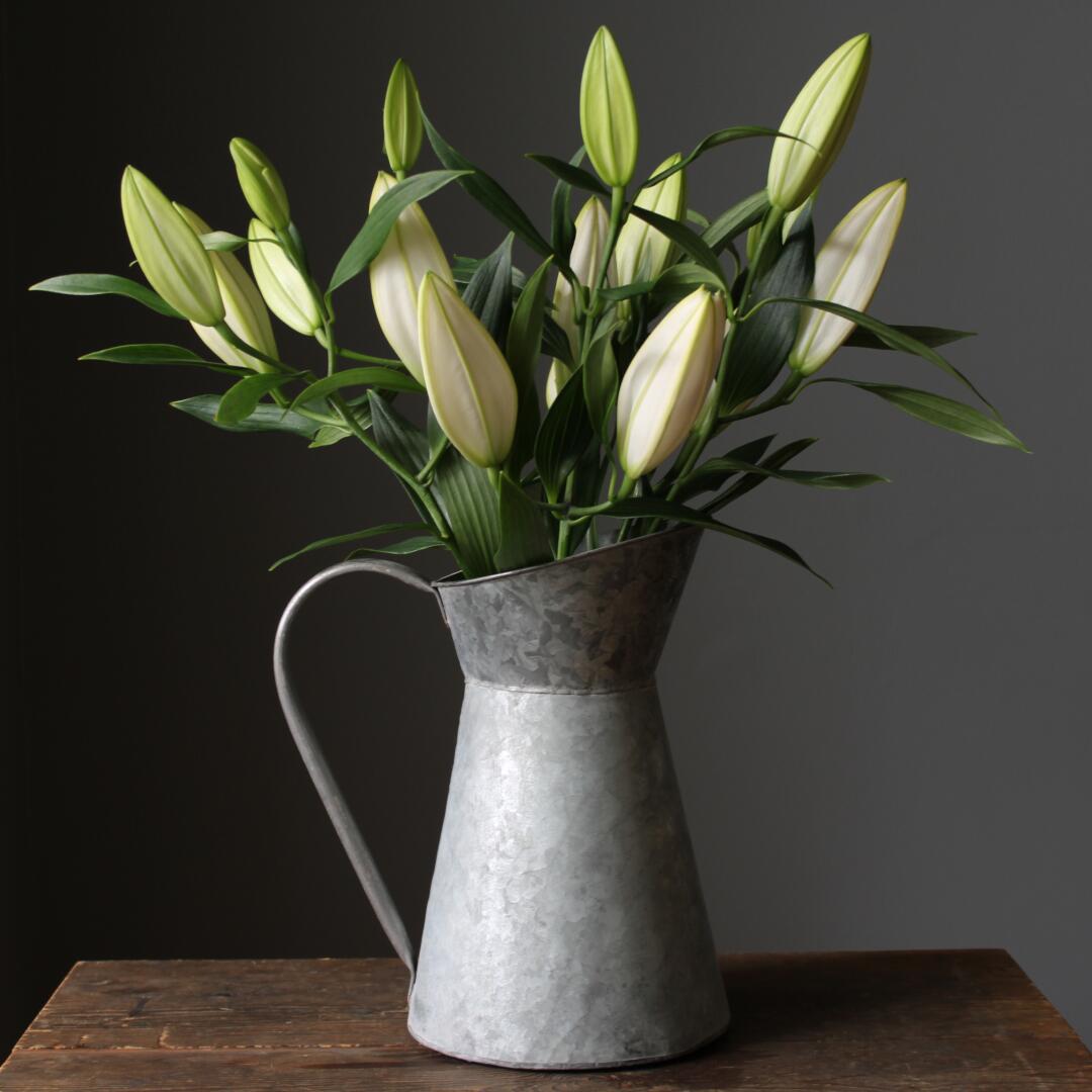 Rustic zinc jug with DIY pot liner used to display a fresh bunch of lilies protecting the jug and table