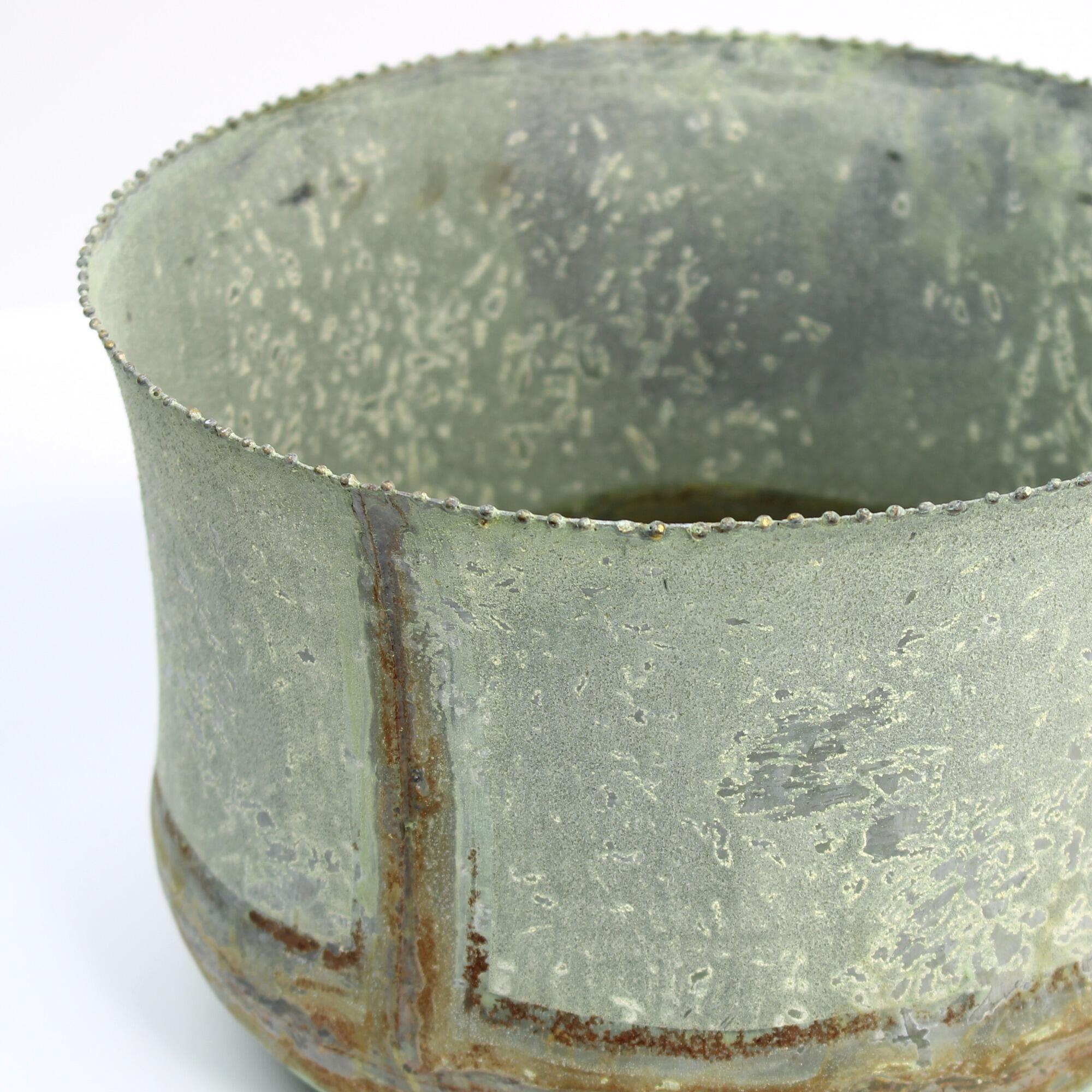 Vintage-style metal planter, close-up showing hand-made seams, weathered verdigris finish, and rusty accents on the base.