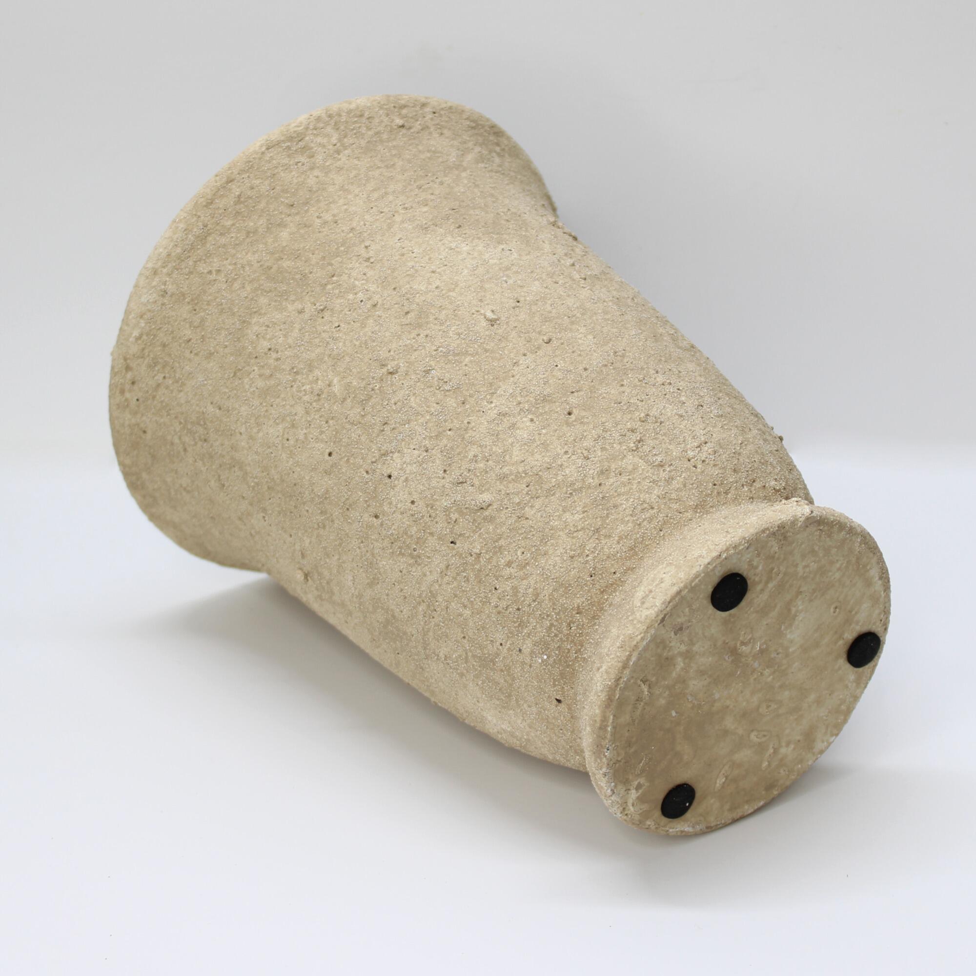 A heavy-duty textured cement pot with a pedestal base on its side, focusing on the base.