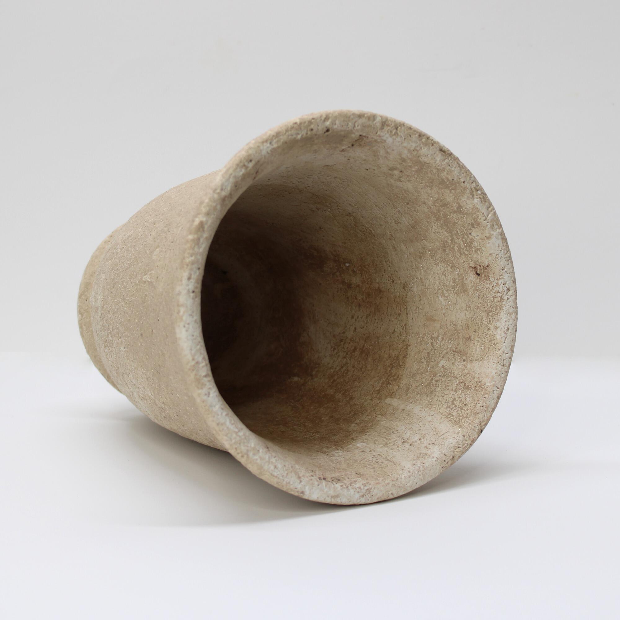 Textured cement pot with a pedestal base with a flared rim.