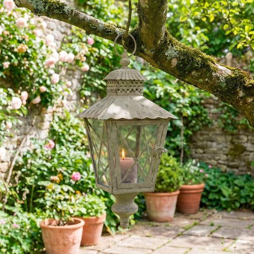 Vintage style candle lantern hanging in the trees in a garden.