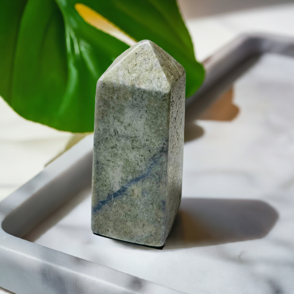 Hackmanite obelisk on a marble tray with a green leaf behind it